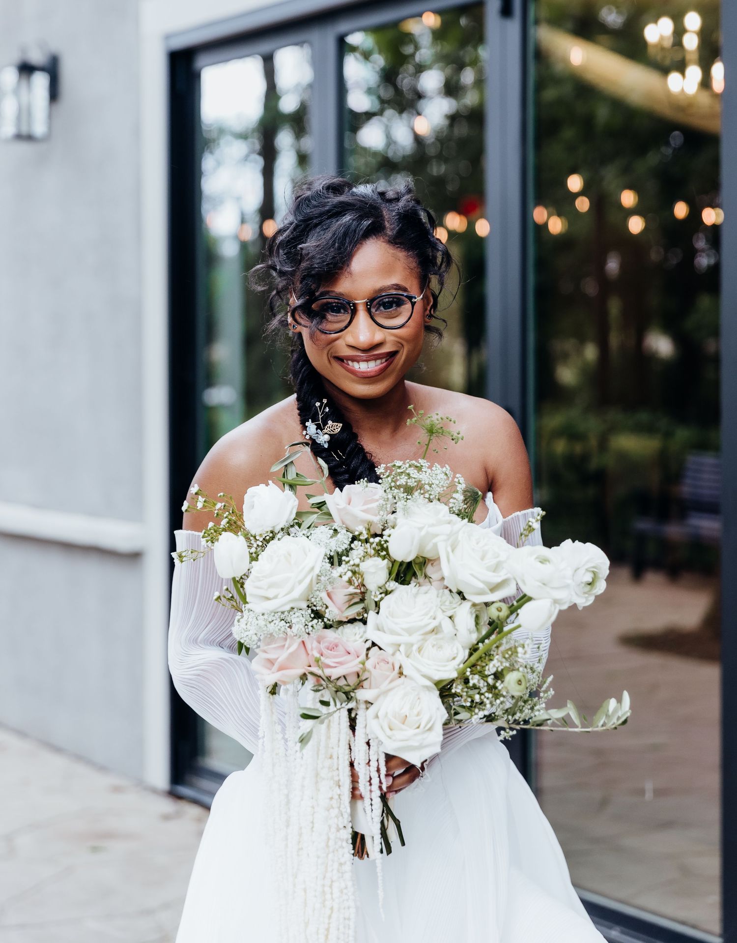 Bride in white dress holding elegant bouquet of white roses and greenery.
