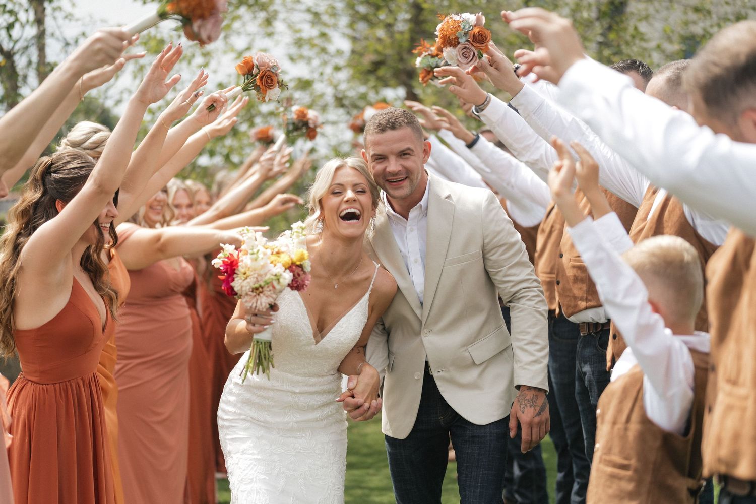 Wedding party celebrates with flower petals being tossed in the air during an outdoor ceremony.