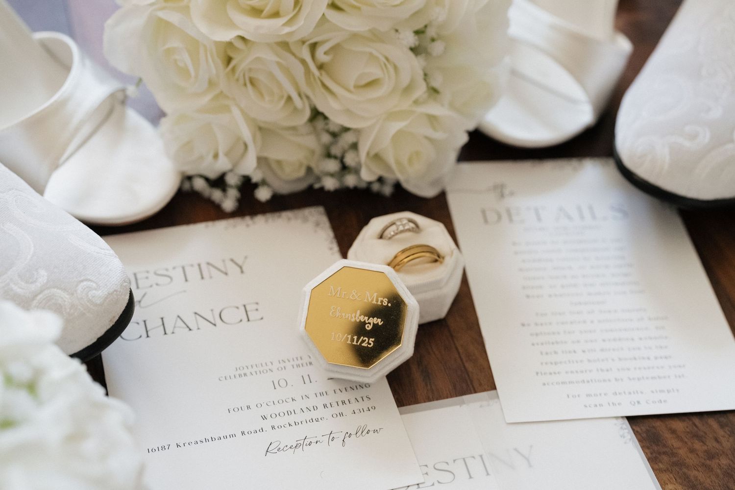 White wedding invitations and envelopes with roses and calligraphy displayed on a dark wooden surface.