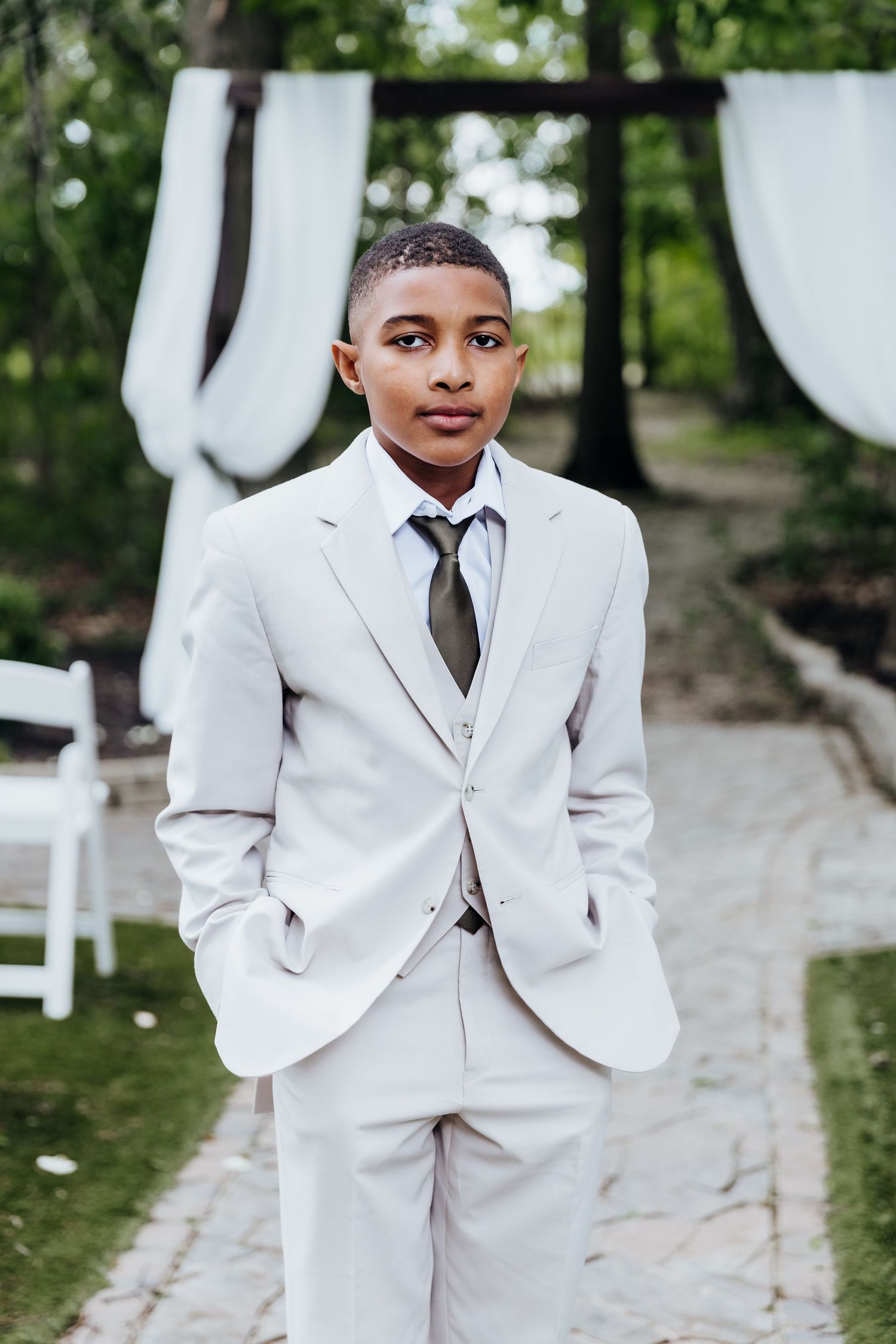 Young attendant in a crisp white suit stands on a stone pathway surrounded by greenery.