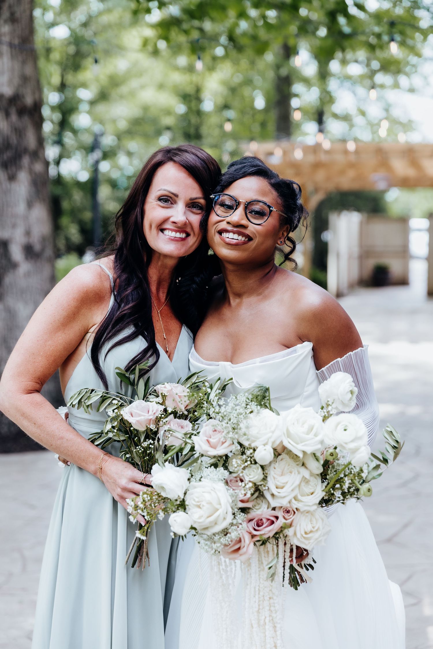 Two bridesmaids in mint green dresses pose with white rose bouquets in a garden setting.