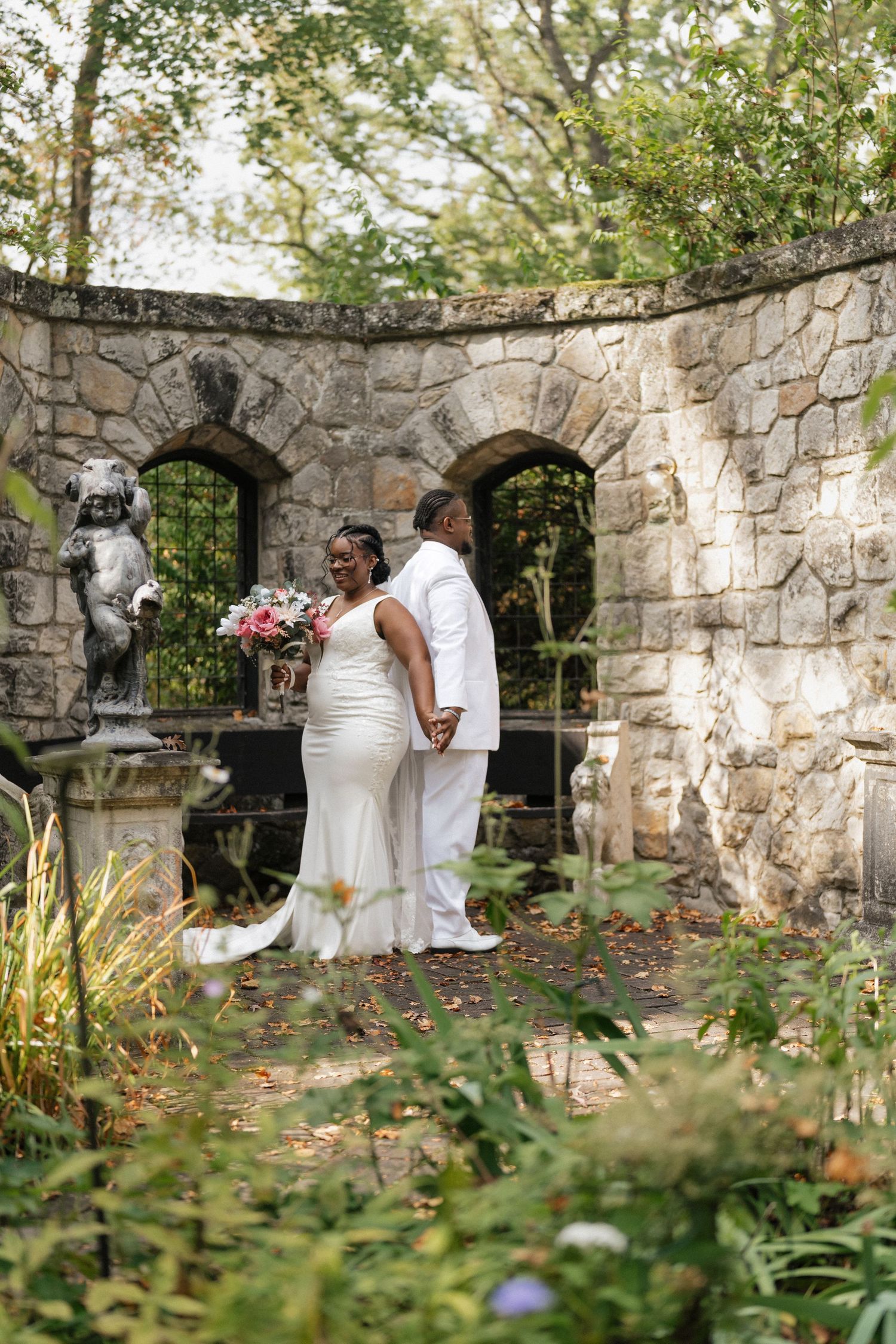 Stone wall garden setting with wedding ceremony participants amid natural greenery and flowers.