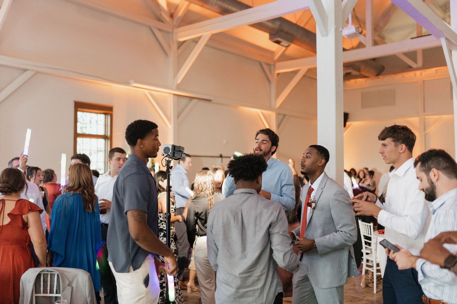 Wedding guests mingling and dancing in bright reception hall with white pillars.
