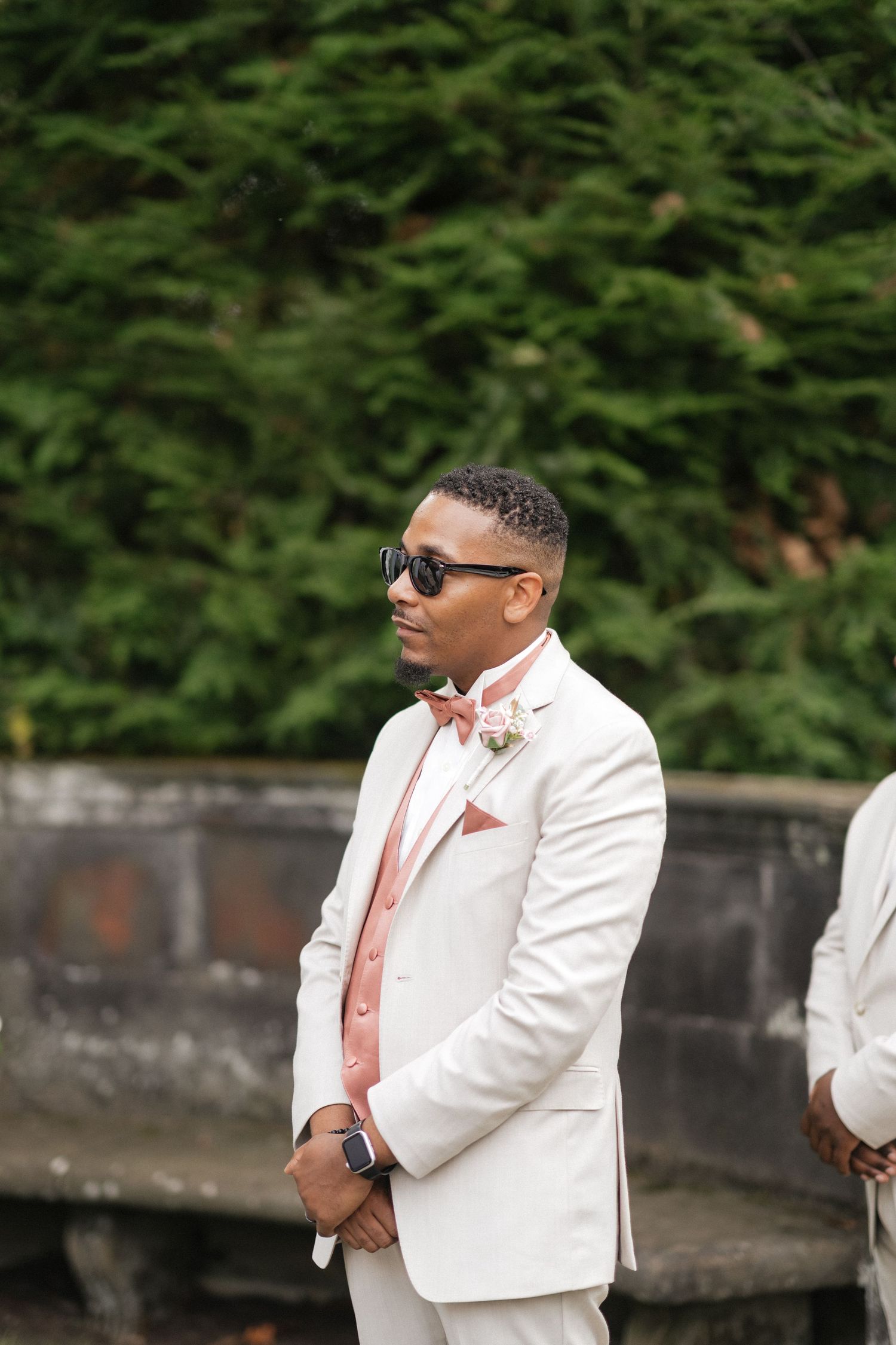 Wedding party members in white suits and sunglasses pose against a natural outdoor backdrop.