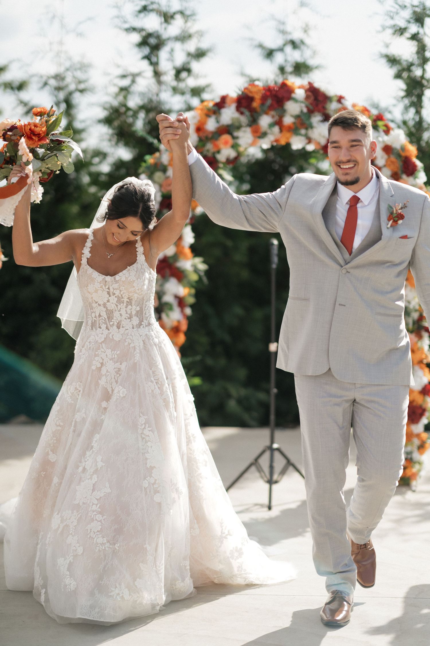 Joyful newlyweds dance and celebrate during their outdoor wedding ceremony with floral arch decorations.