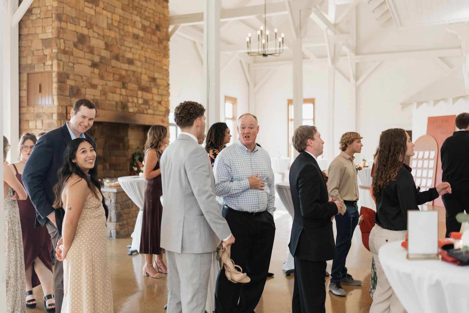 Wedding guests mingle in elegant brick-walled venue decorated with white and red accents.
