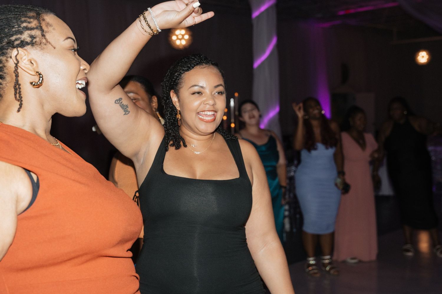 Wedding guests dance together under purple mood lighting at reception.