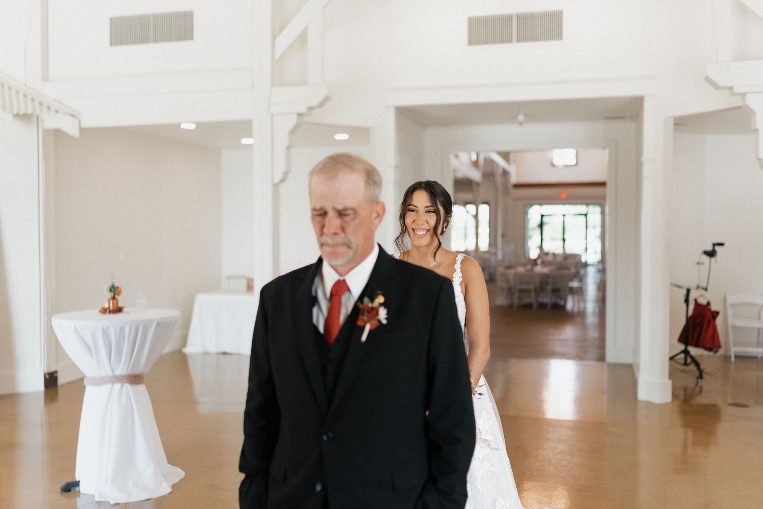 Wedding party members walk through an elegant white indoor venue with tall columns and hardwood floors.