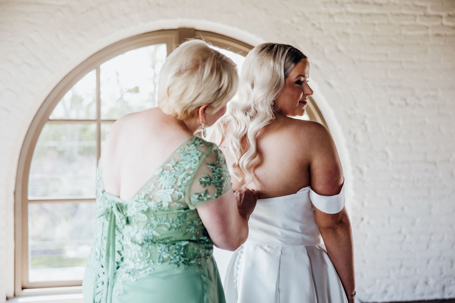 Wedding party wearing sage green dresses standing together in a bright venue.