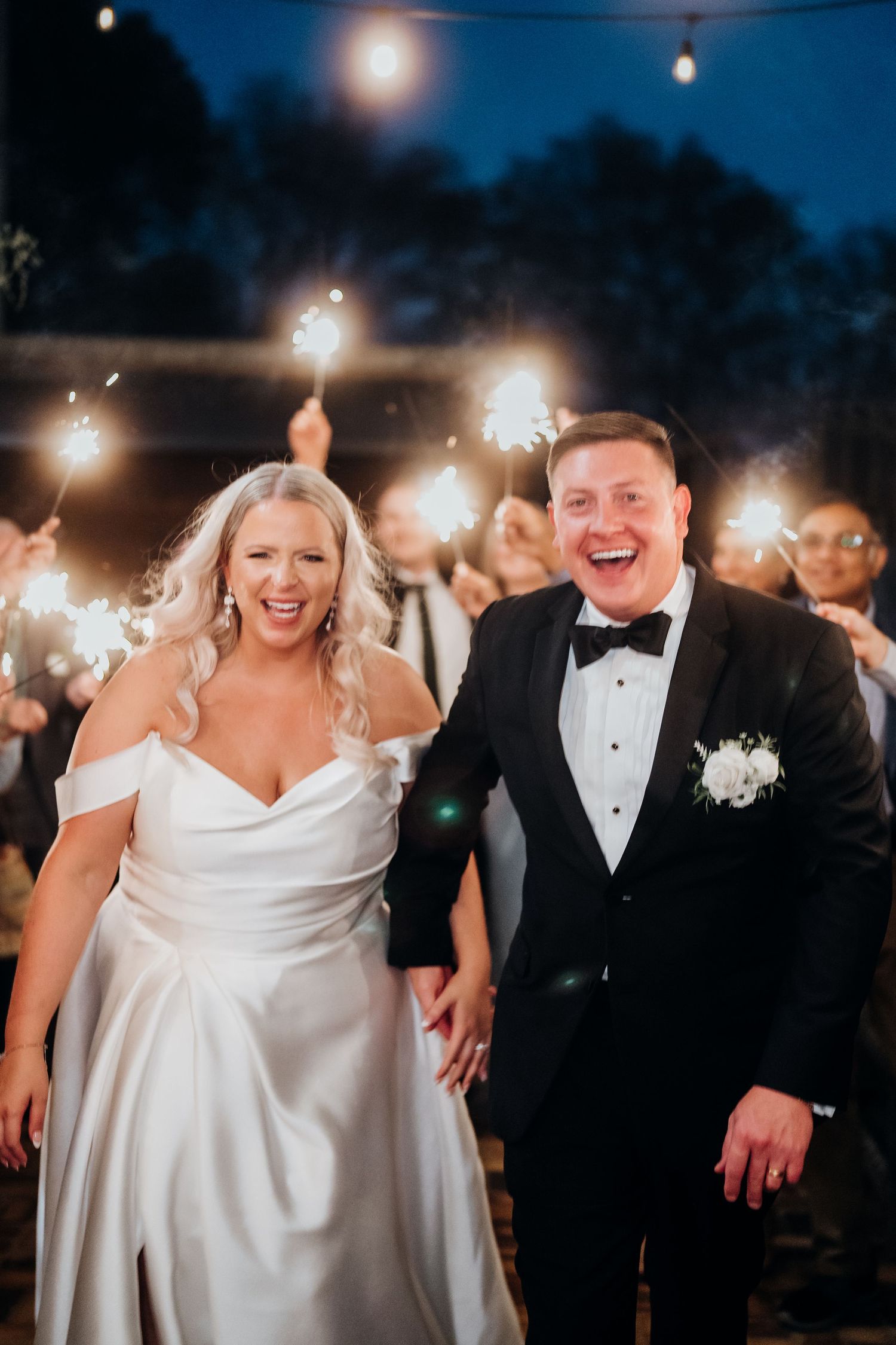 Newlyweds celebrate under sparklers at nighttime wedding reception.