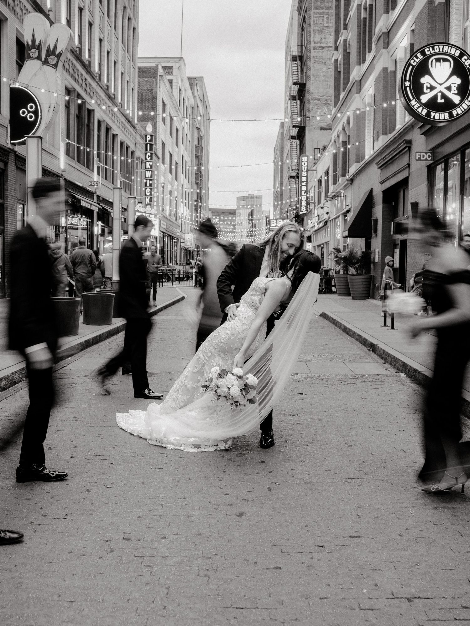 Black and white photo of wedding festivities on an urban street with vintage storefronts.