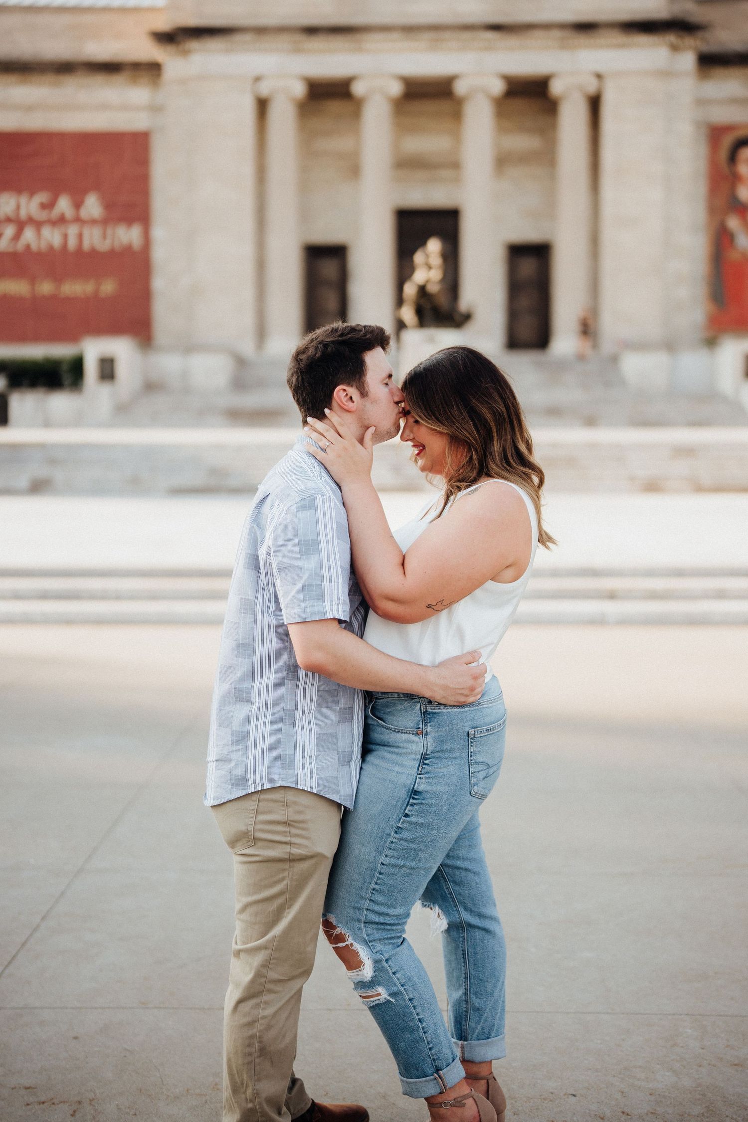 A tender moment captured between a couple standing in front of a museum building.