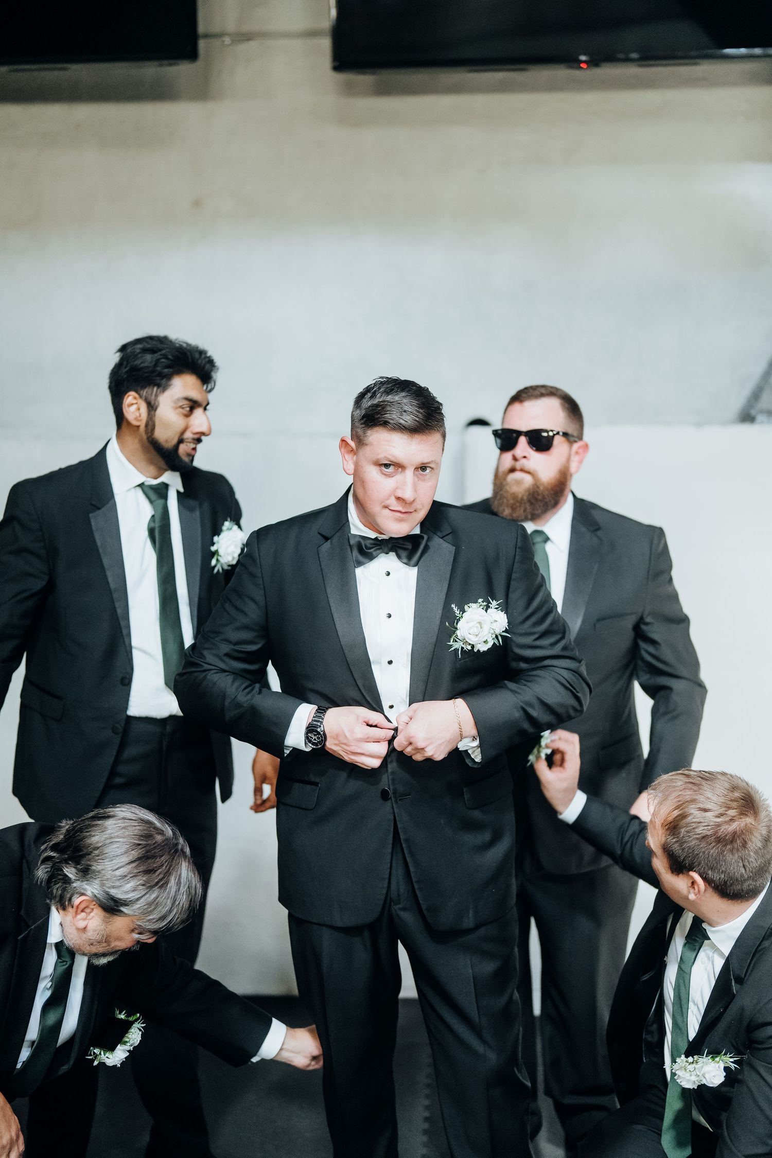 Wedding party members in formal black tuxedos share a candid moment together.