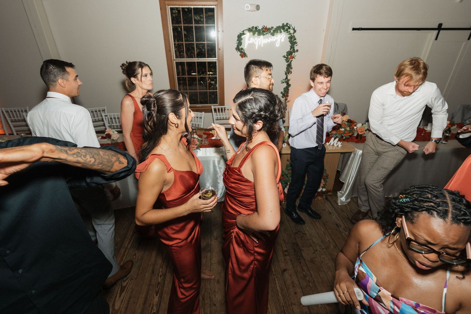 Wedding guests dancing and socializing at an indoor reception with burgundy attire.