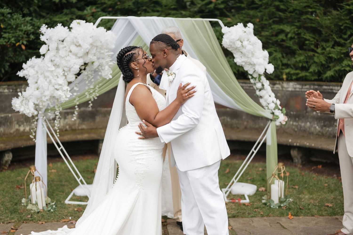 Romantic wedding ceremony moment under white floral arch with flowing fabric drapes.