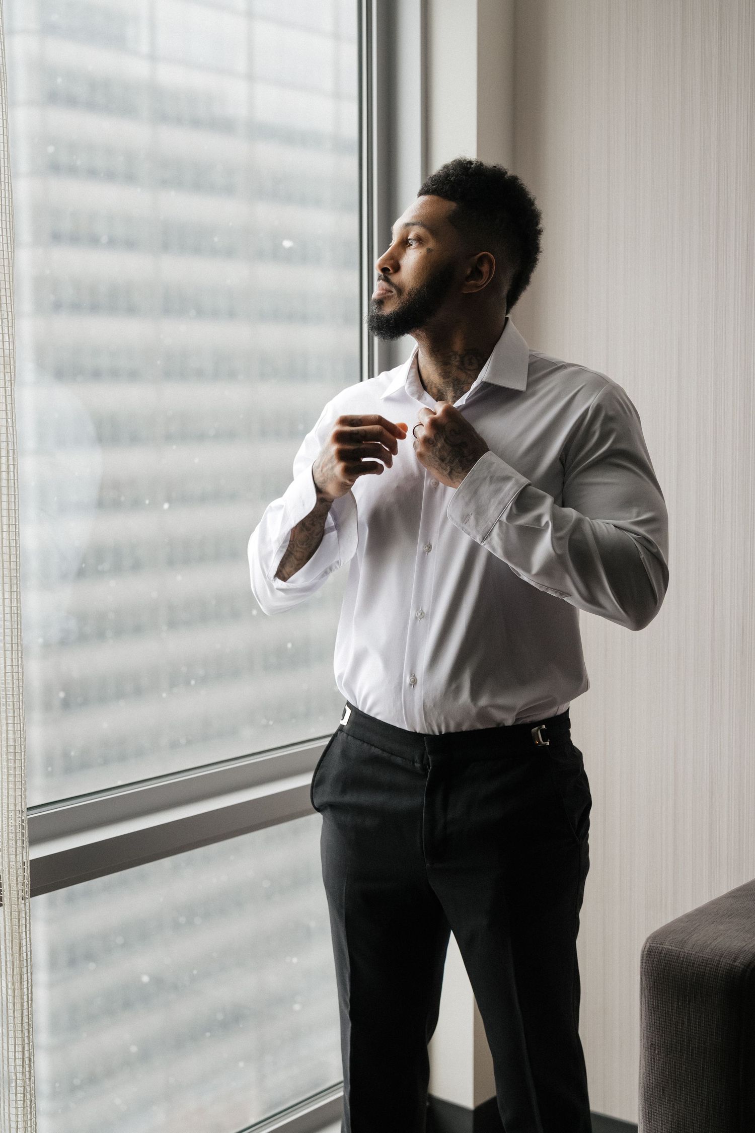 Person in white dress shirt and black pants stands by window in office, looking contemplative in three poses.