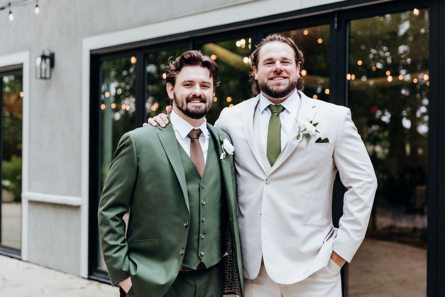 Three groomsmen smile together in formal attire with one wearing a dark green suit between two in white.