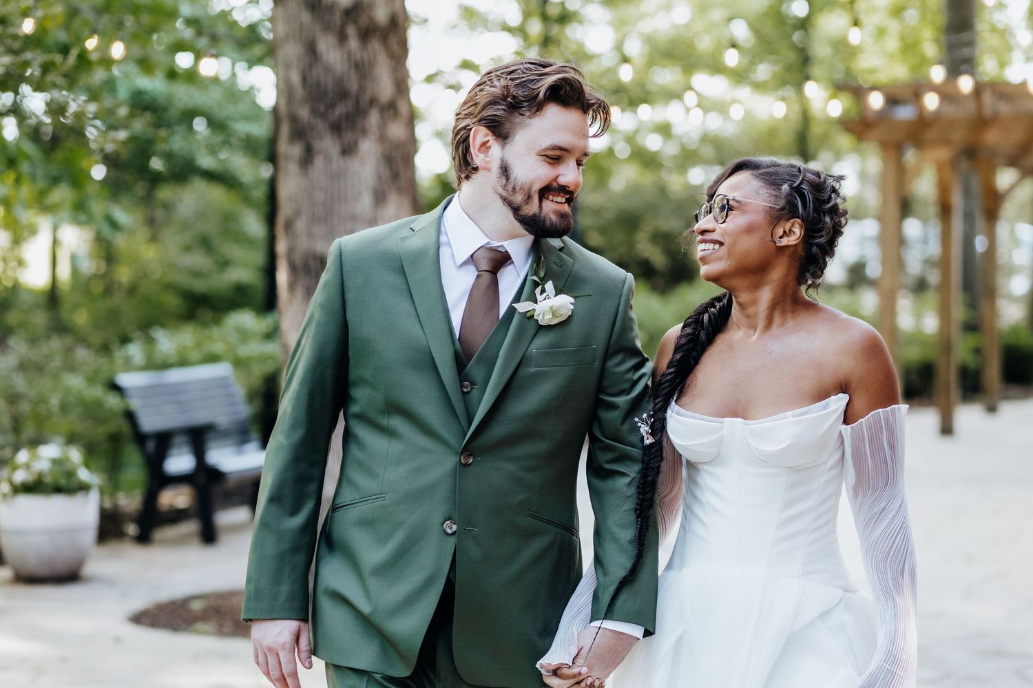 Elegant couple in green suit and white wedding dress share romantic moments in outdoor setting.
