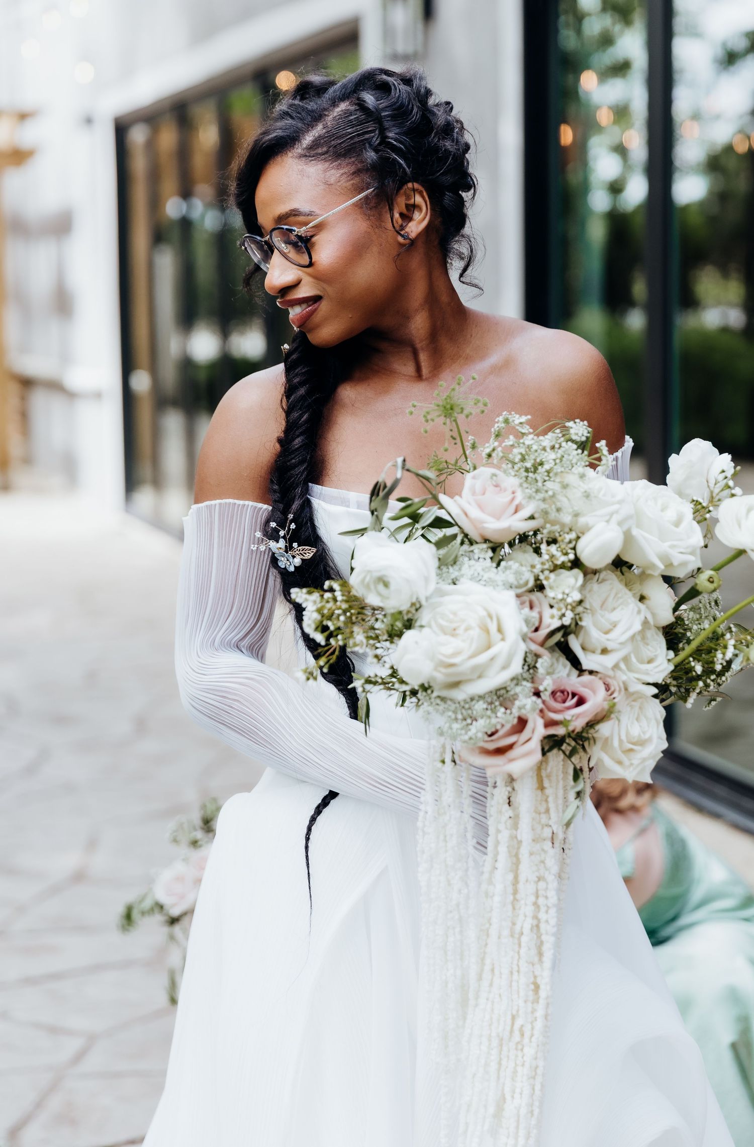 A bride with glasses holds an elegant white rose bouquet with cascading ribbons.