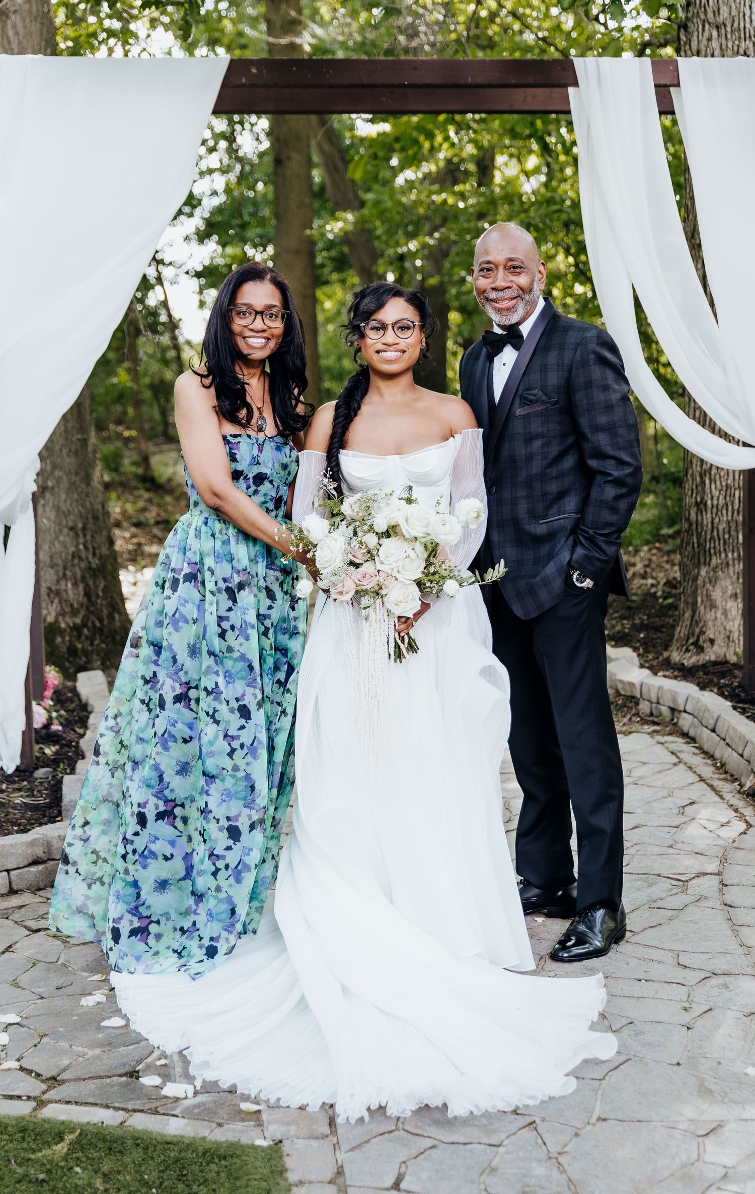 Wedding party poses outdoors with bride in white gown and bridesmaid in floral blue dress.