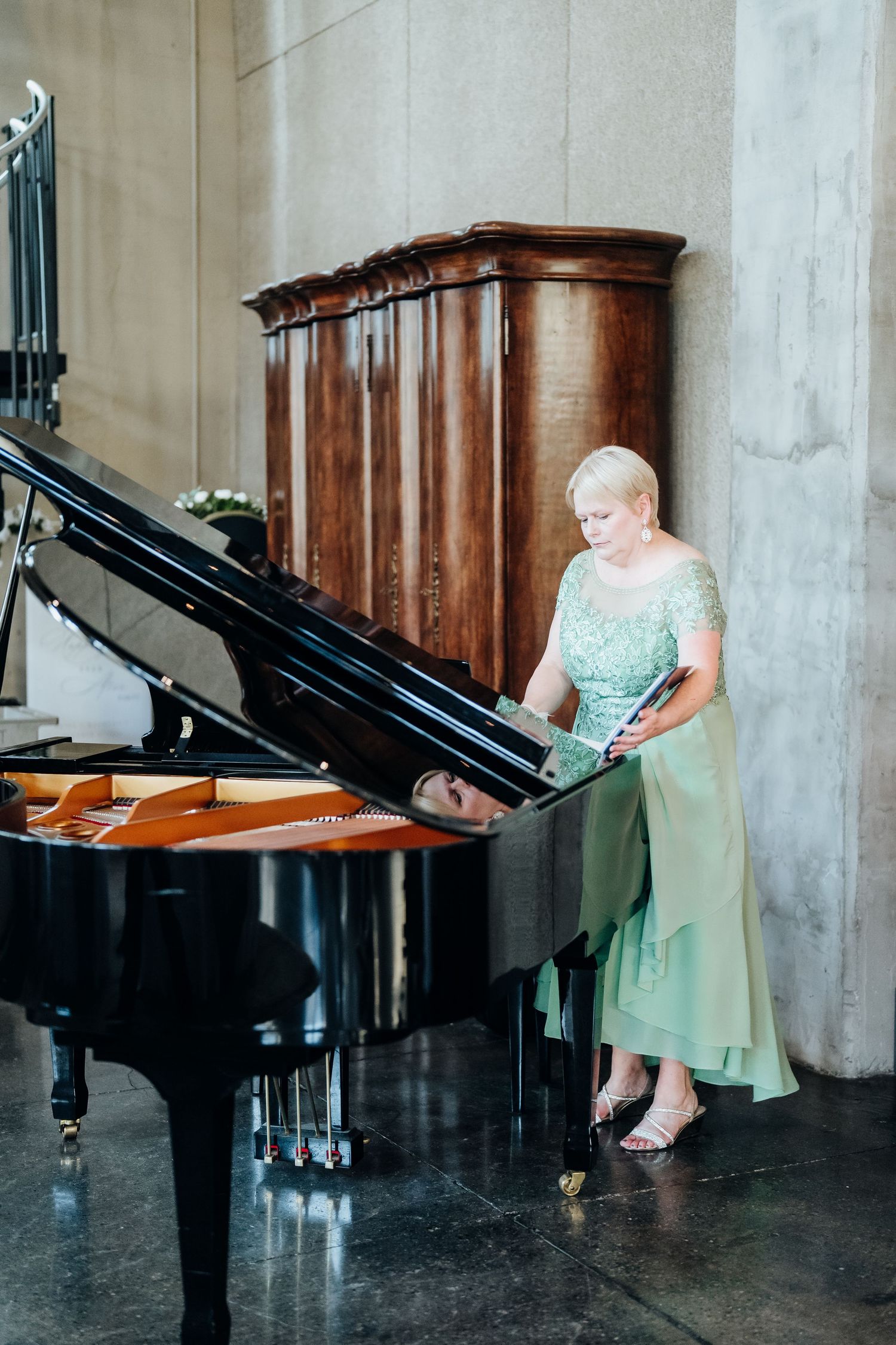 A person in a mint green dress sits at a grand piano in an elegant venue.