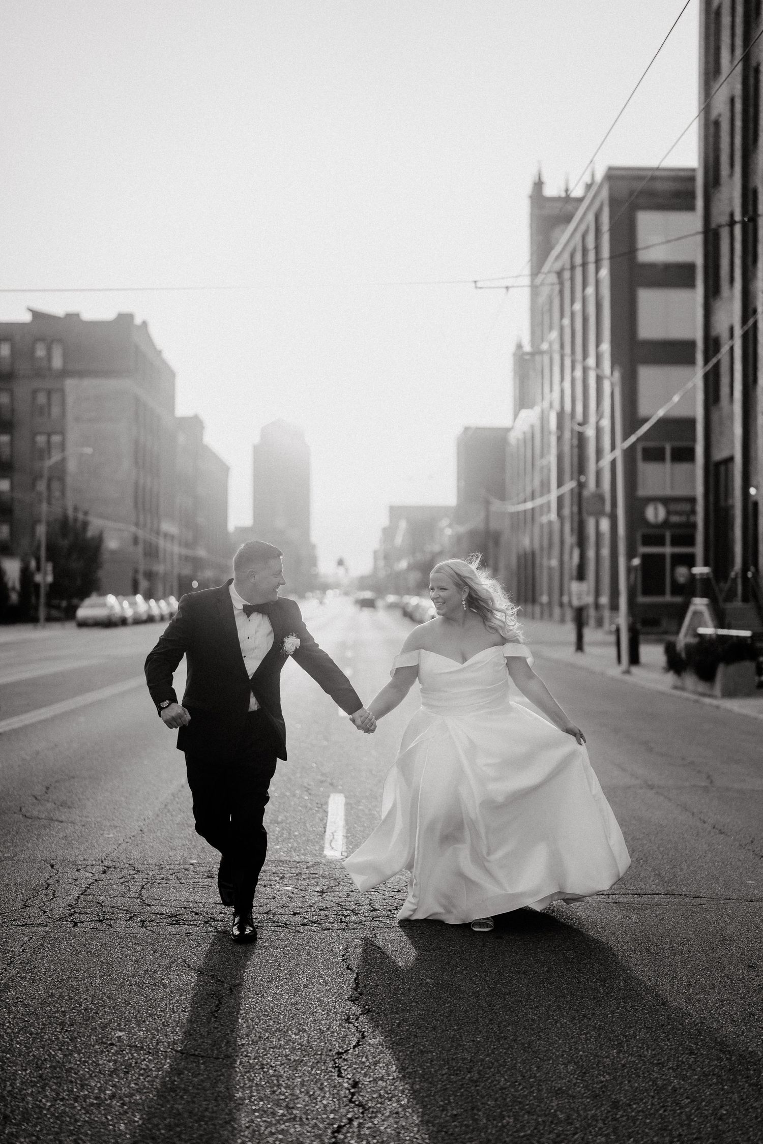 Black and white photo of couple running playfully down an urban street.