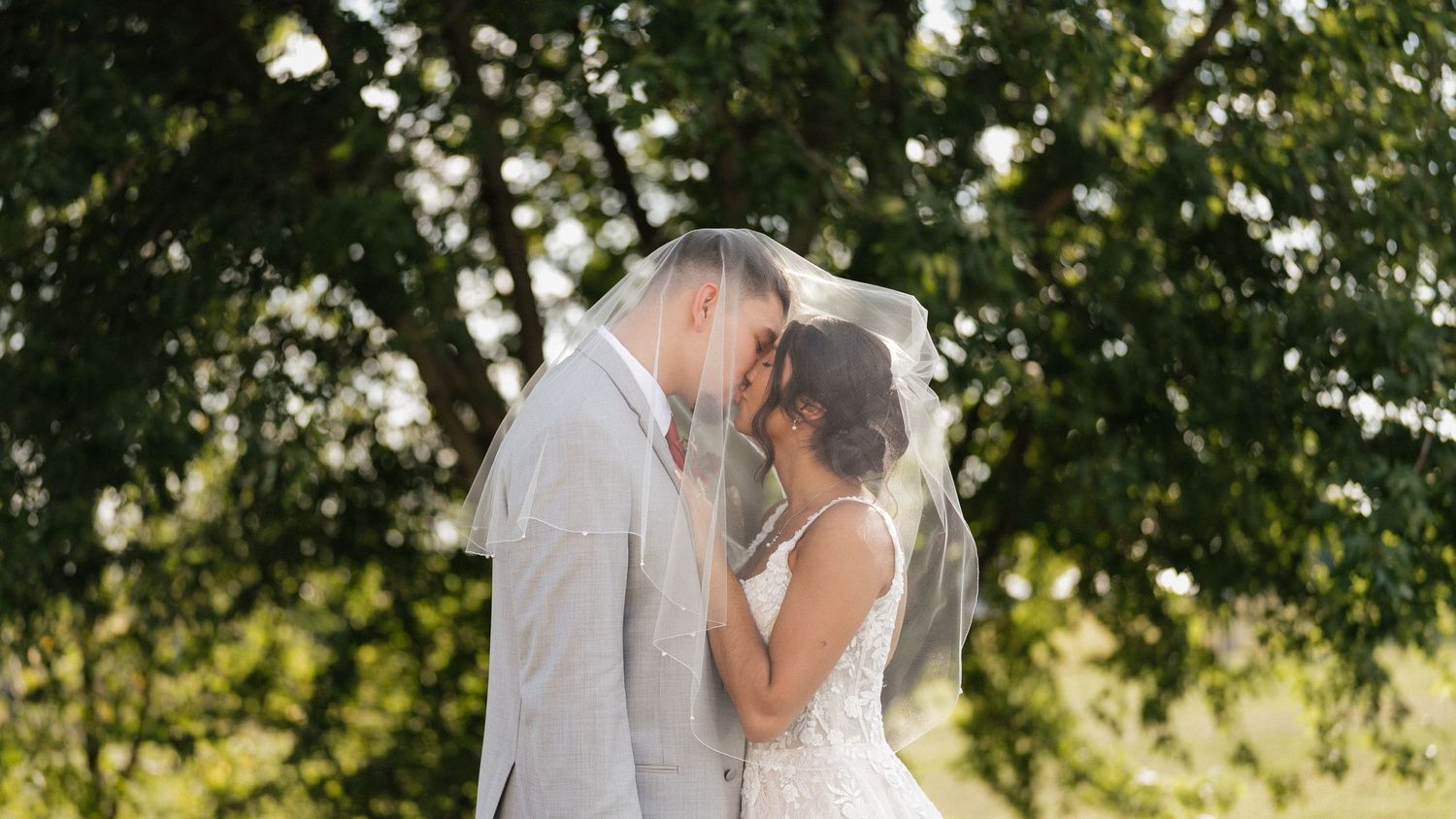 A couple shares a romantic moment under tree branches in their wedding attire.