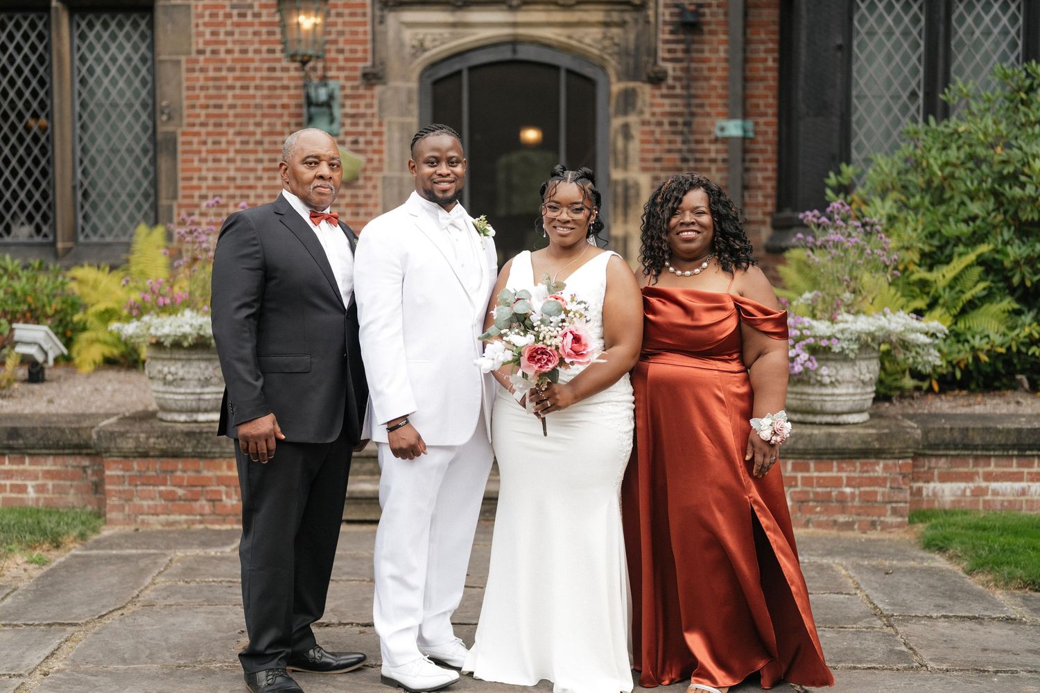 Wedding party members pose in front of a brick building with white and rust-colored attire.