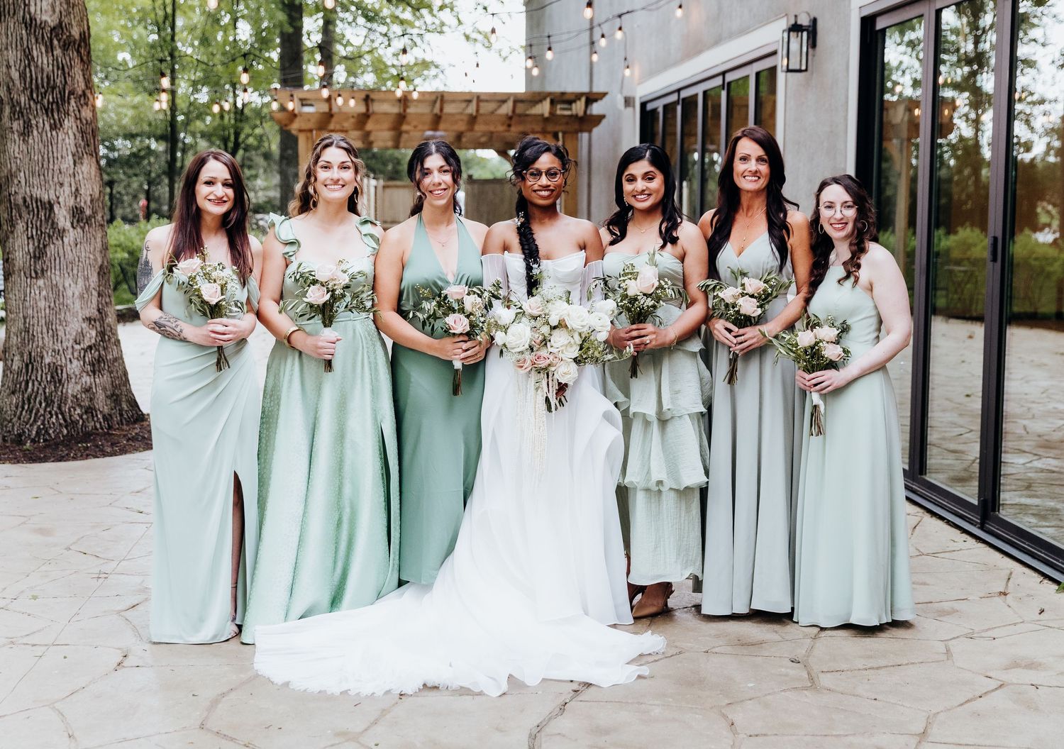 Bridesmaids in mint green dresses pose with bride in white gown holding floral bouquets.