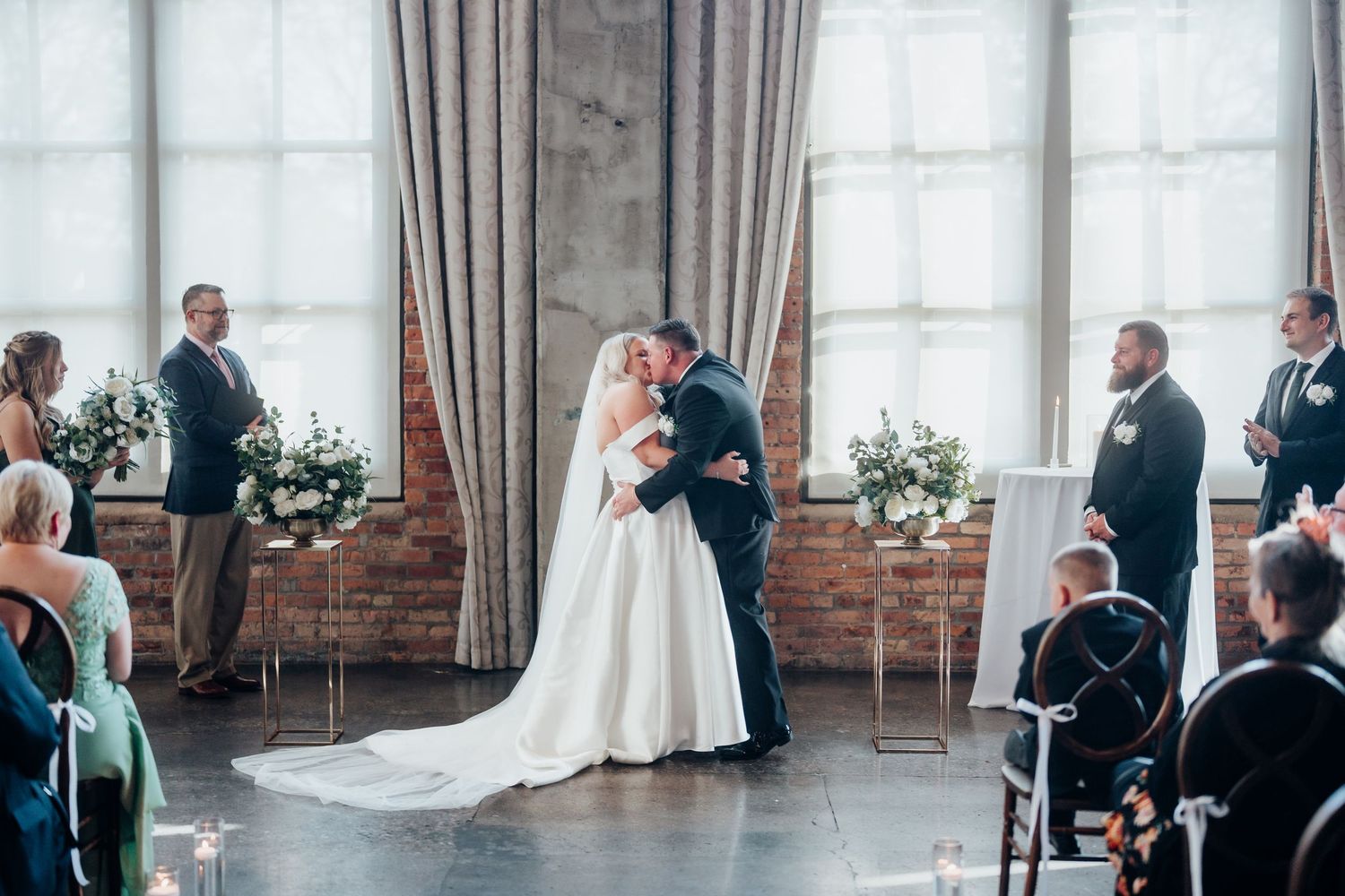 Wedding ceremony setup in an industrial venue with exposed brick walls and large windows.