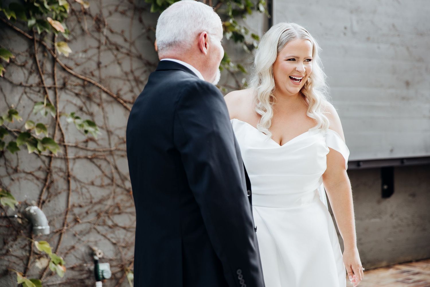 Emotional first look between couple in wedding attire against white brick wall.