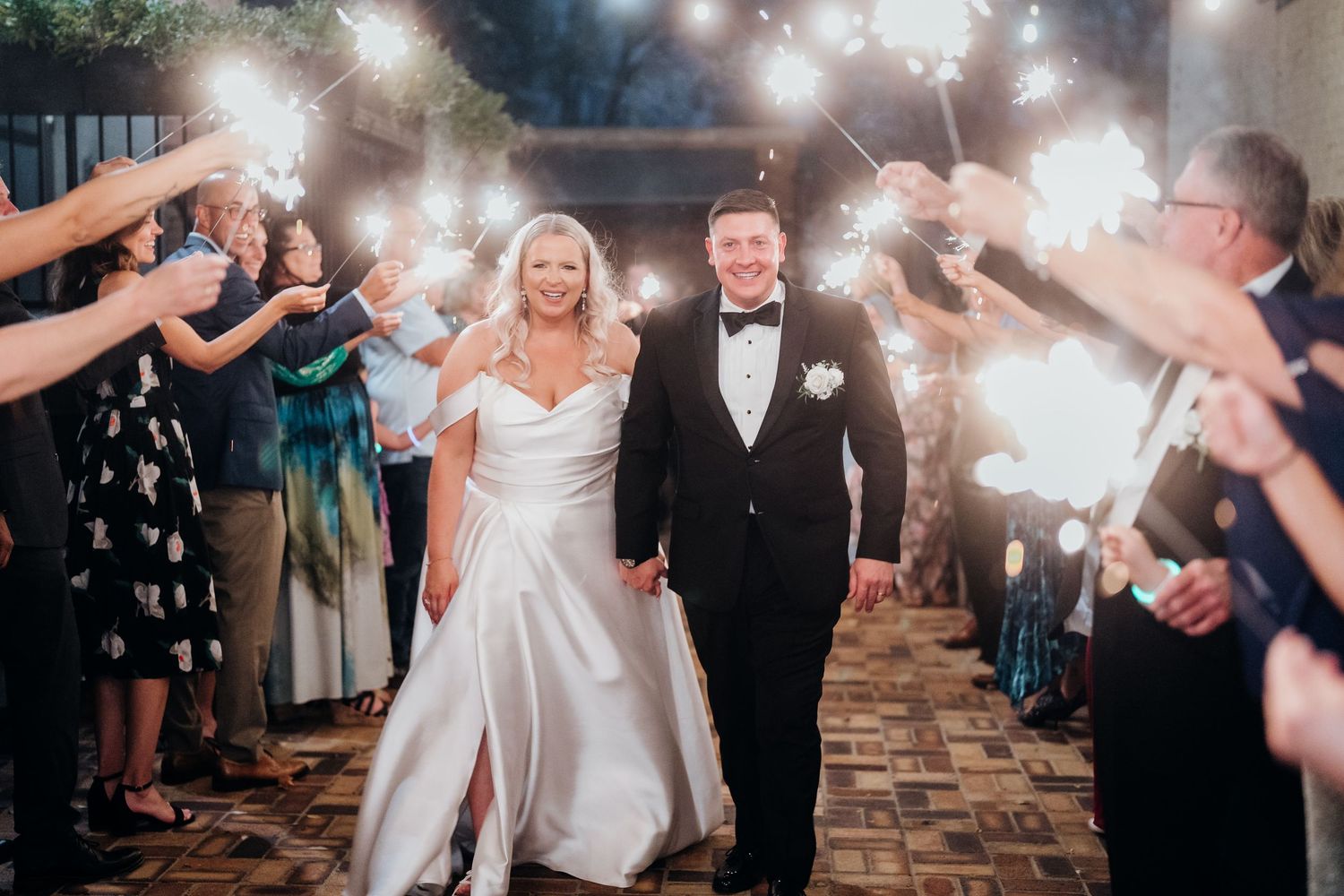 Wedding couple walks through sparkler exit line during evening celebration.