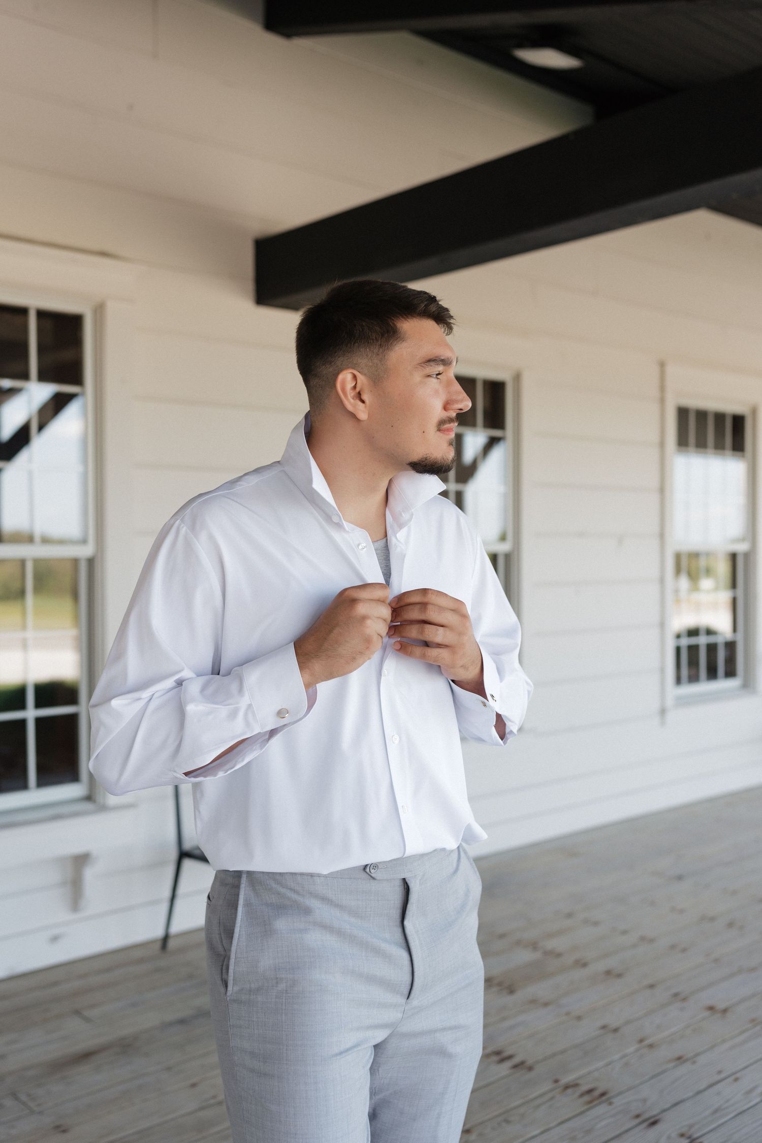 Person in light gray suit and white shirt adjusting their collar outdoors.