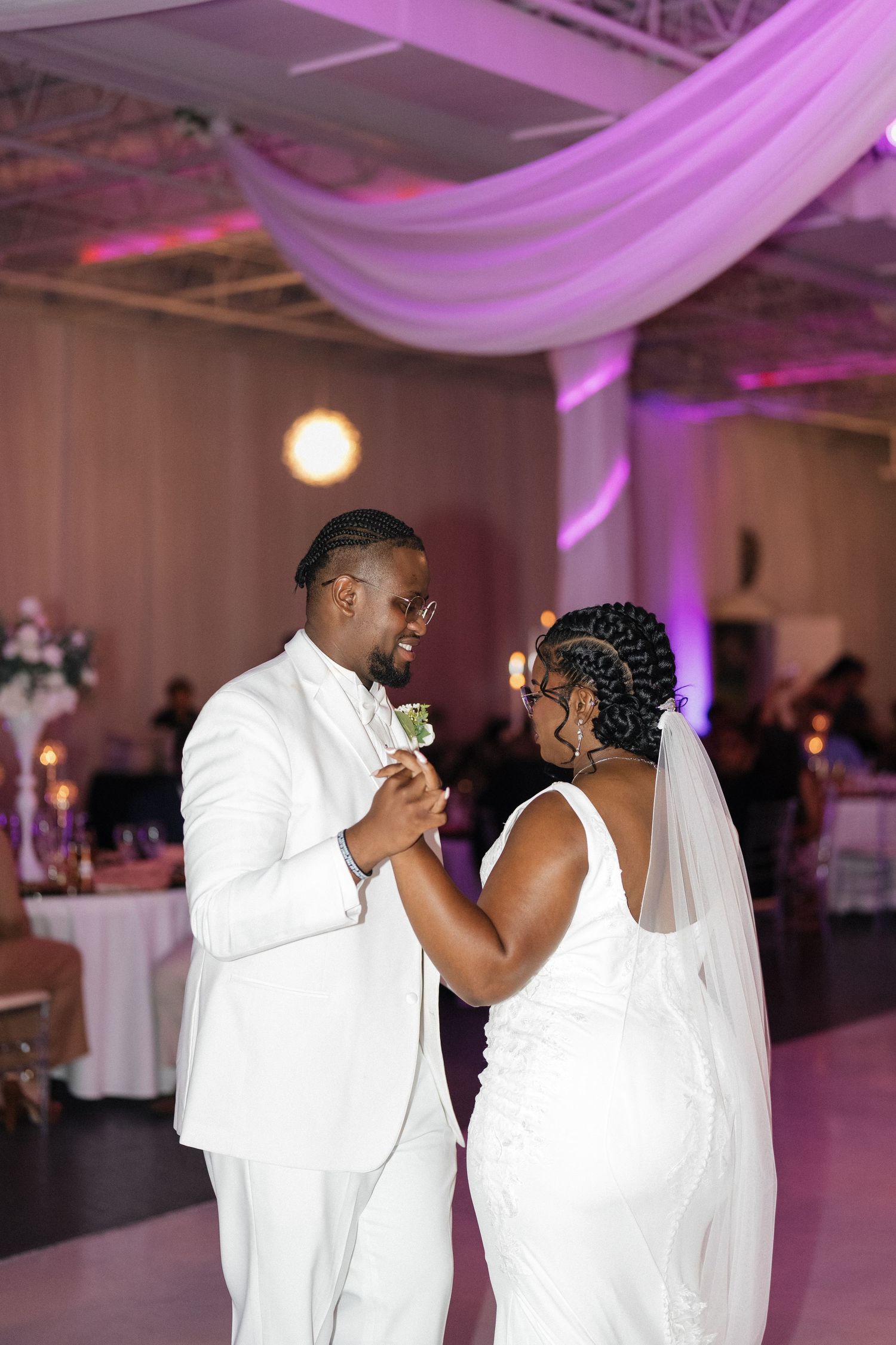 Couple shares their first dance under purple-lit draping in an elegant reception hall.