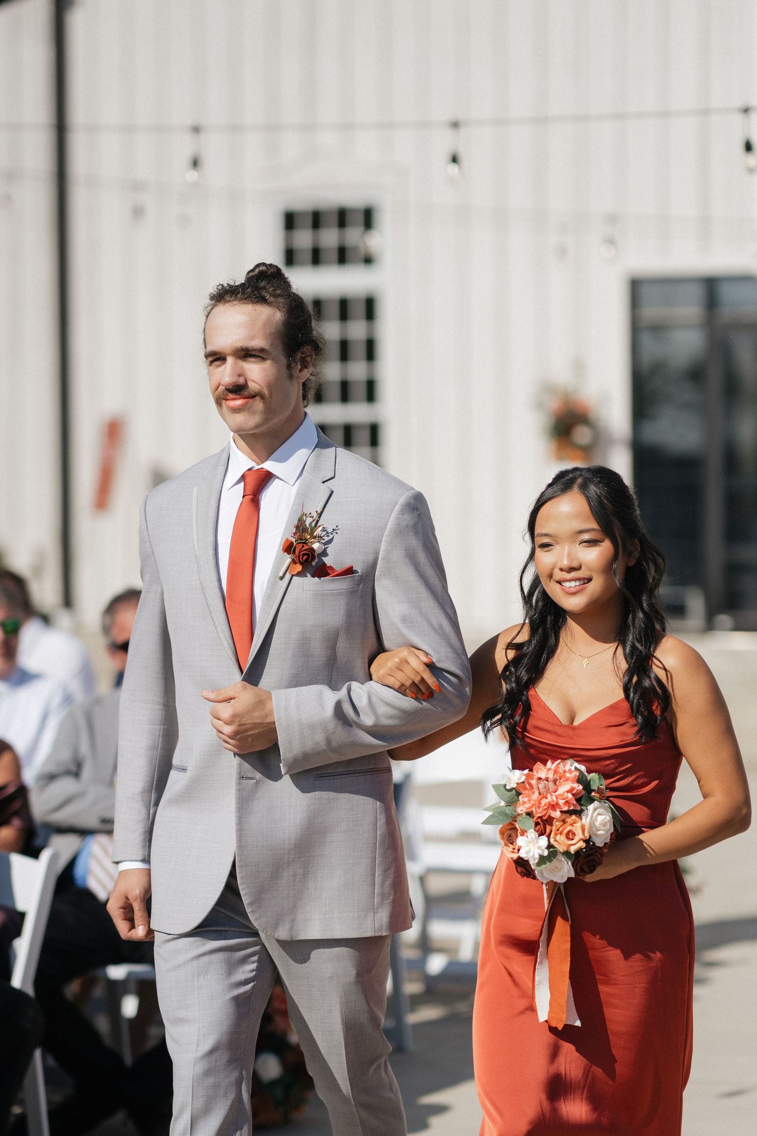 Wedding party members in gray suits and coral dresses walking and laughing together.