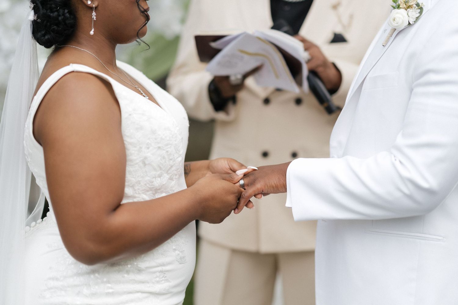 Wedding ceremony participants exchange rings in white formal attire.