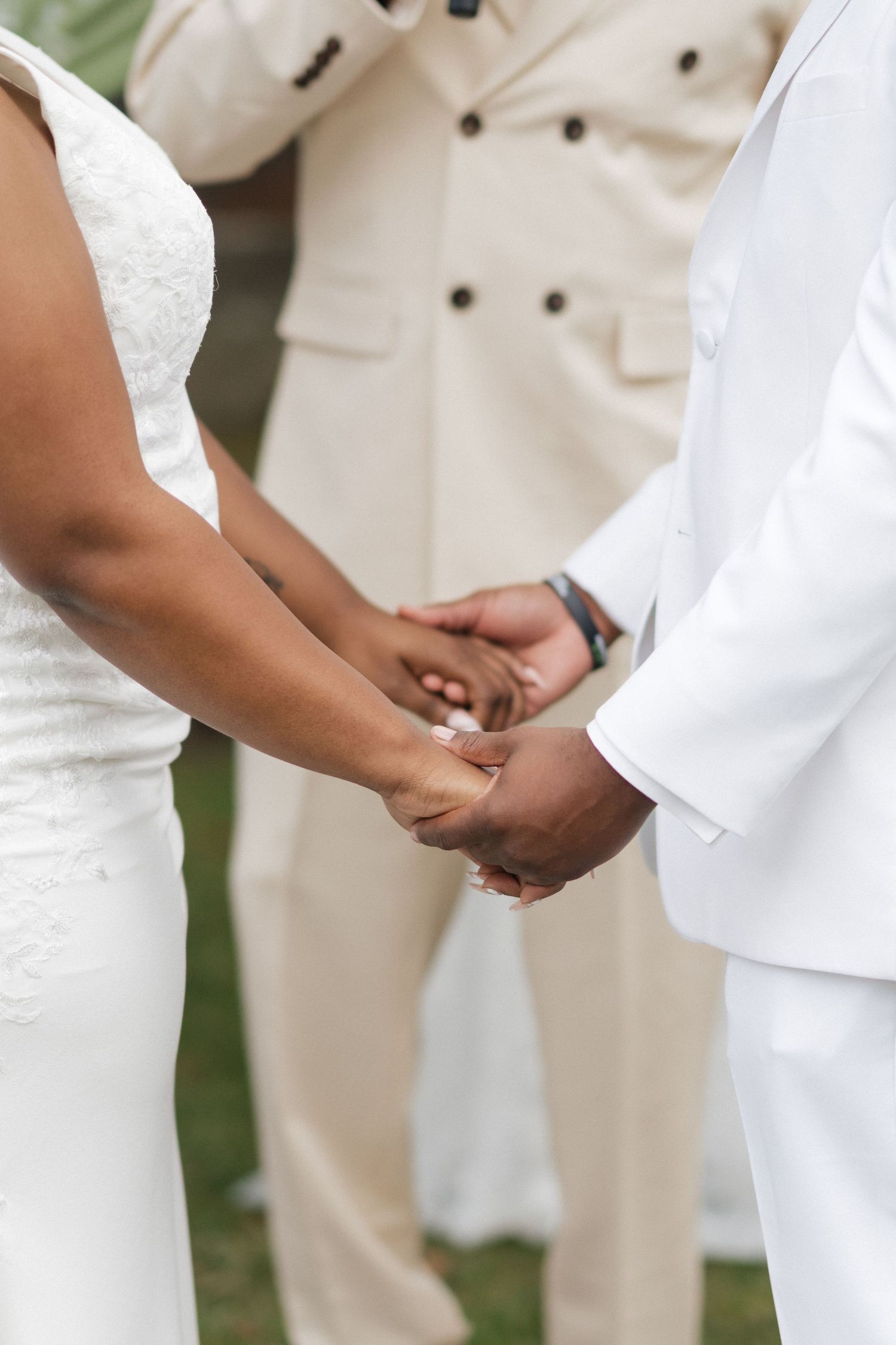 Wedding ceremony detail showing hands clasped together with white and beige formal attire.