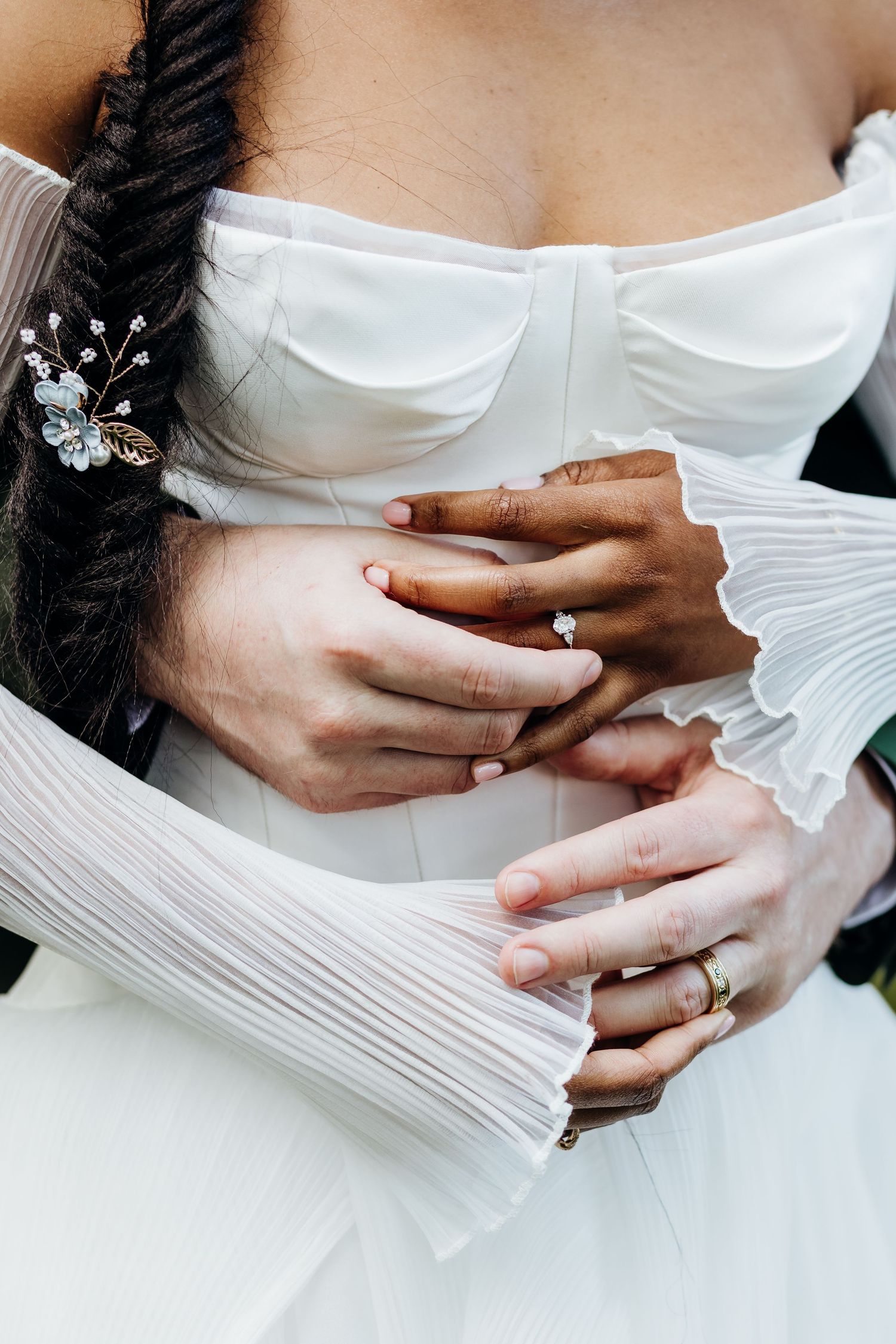 Close-up detail of wedding dress bodice and hands showing engagement ring and bridal accessories.