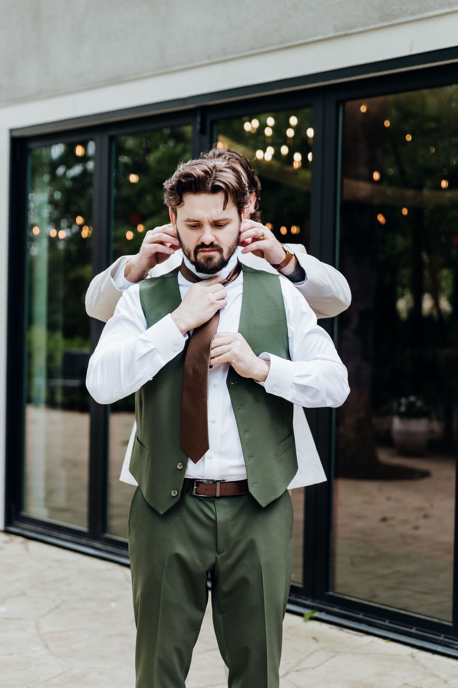 Groom in olive green vest and white shirt adjusts his bowtie in a series of preparation shots.