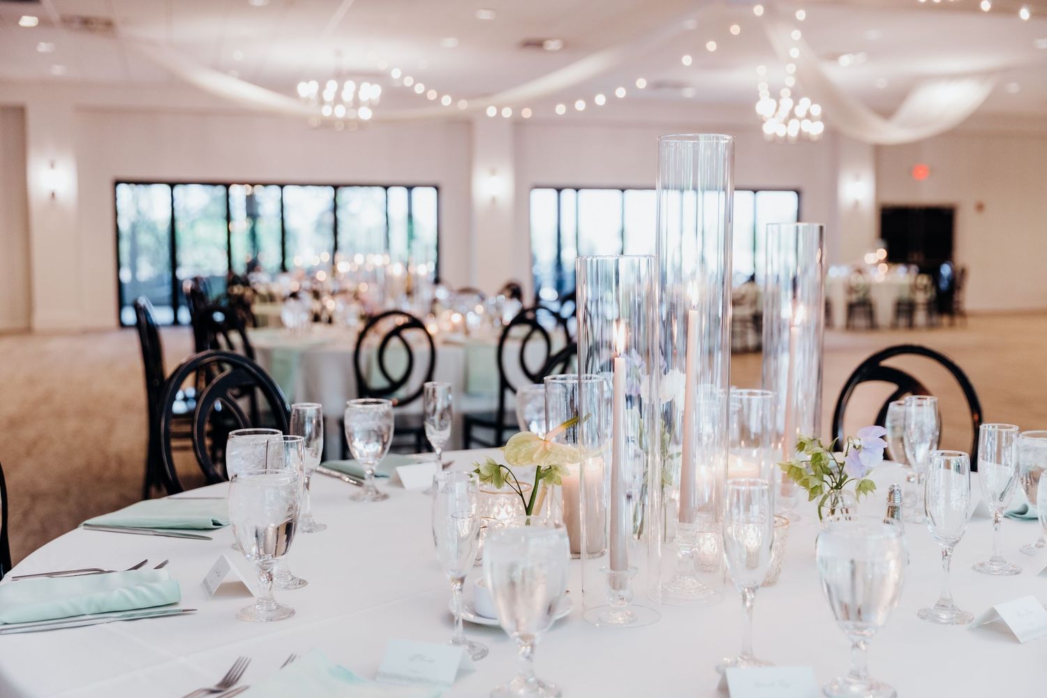 An elegant wedding reception hall with string lights and table settings.