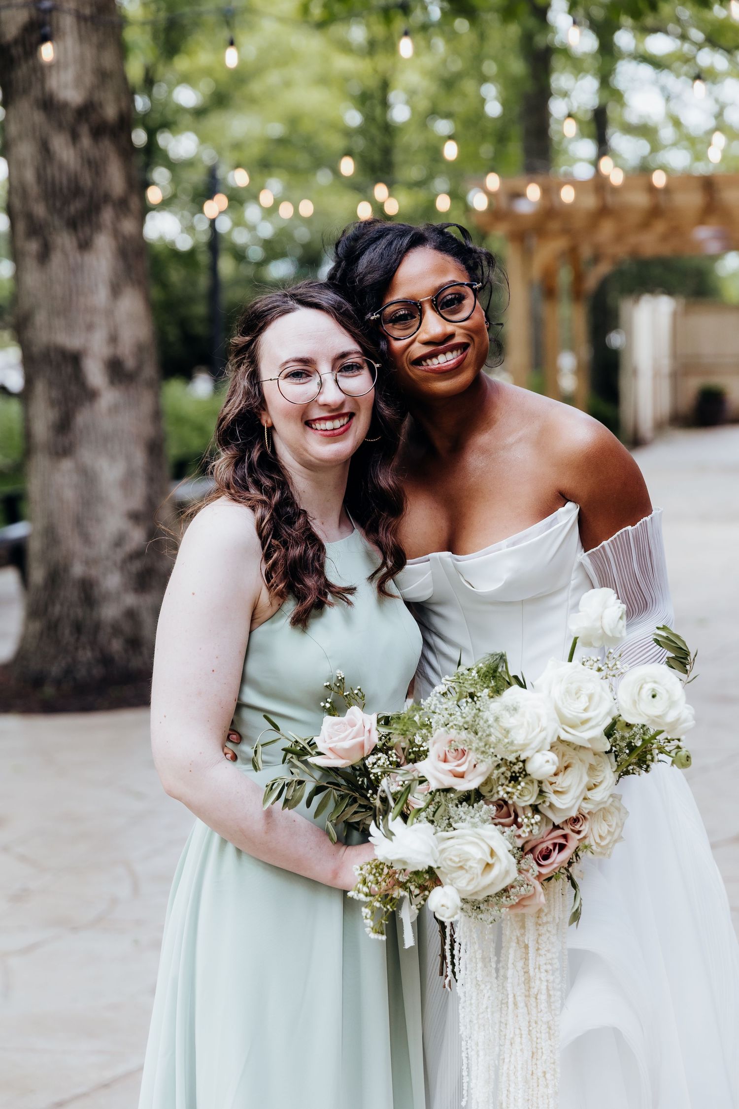 Wedding party members in mint green dresses hold elegant white floral bouquets outdoors.