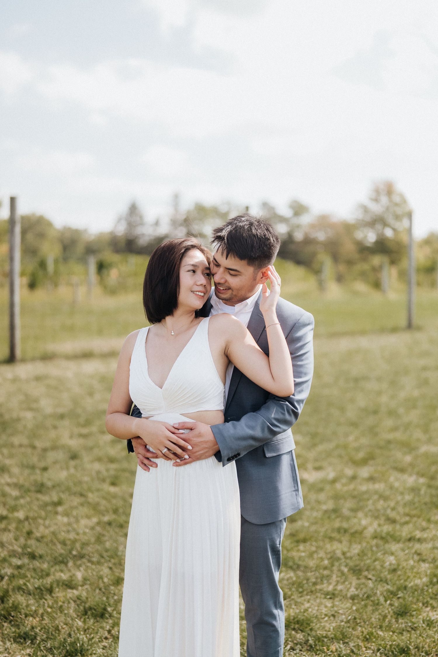 Intimate moment between couple in wedding attire embracing in sunny outdoor field.