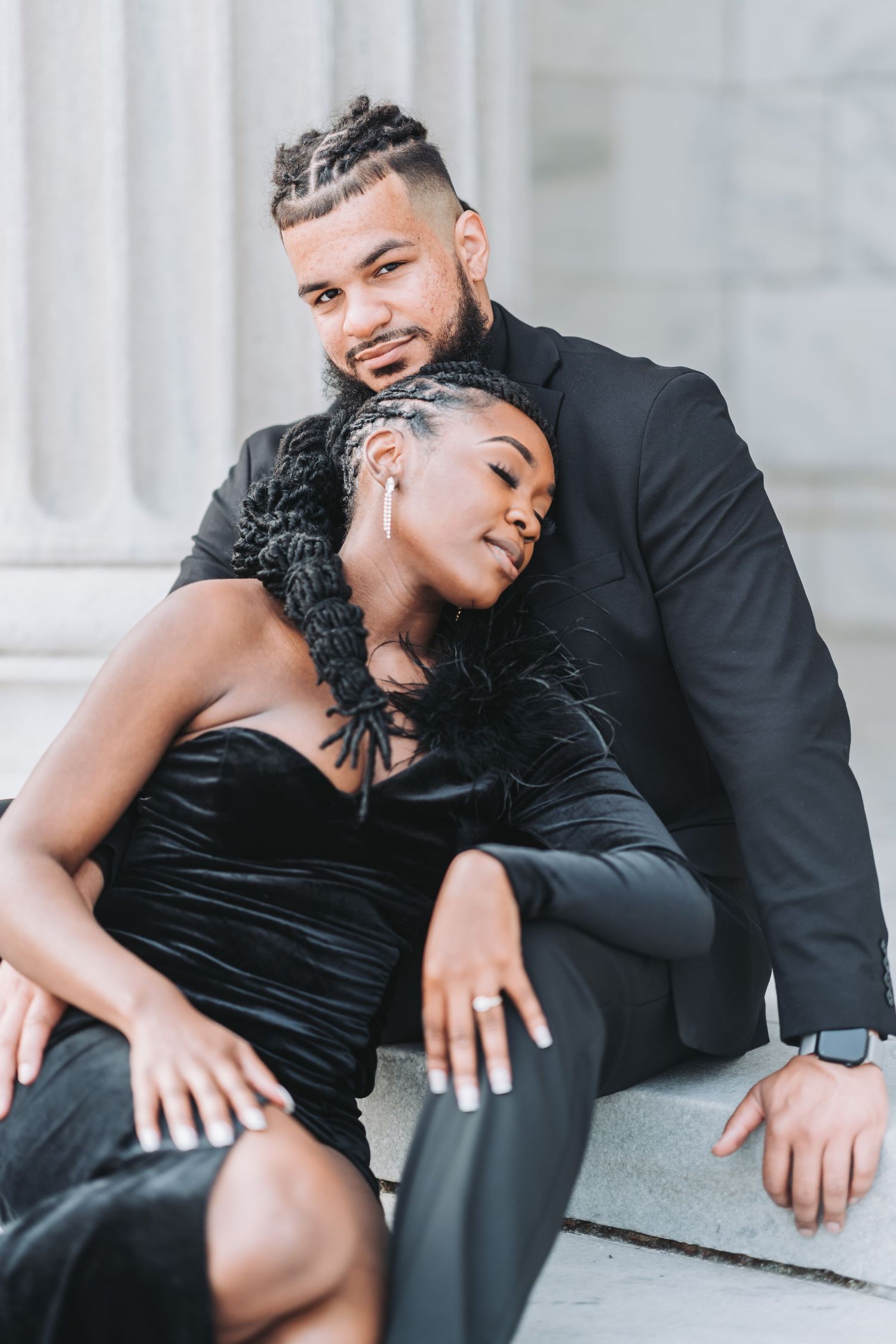 A stylish couple poses intimately against a classical column backdrop in matching black formal wear.