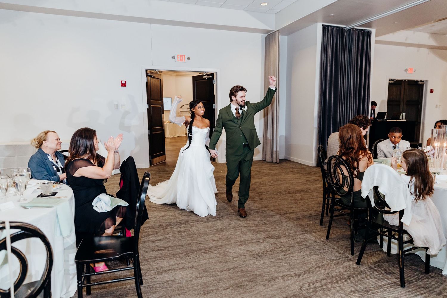 Indoor wedding reception venue with guests seated at tables with black chairs.