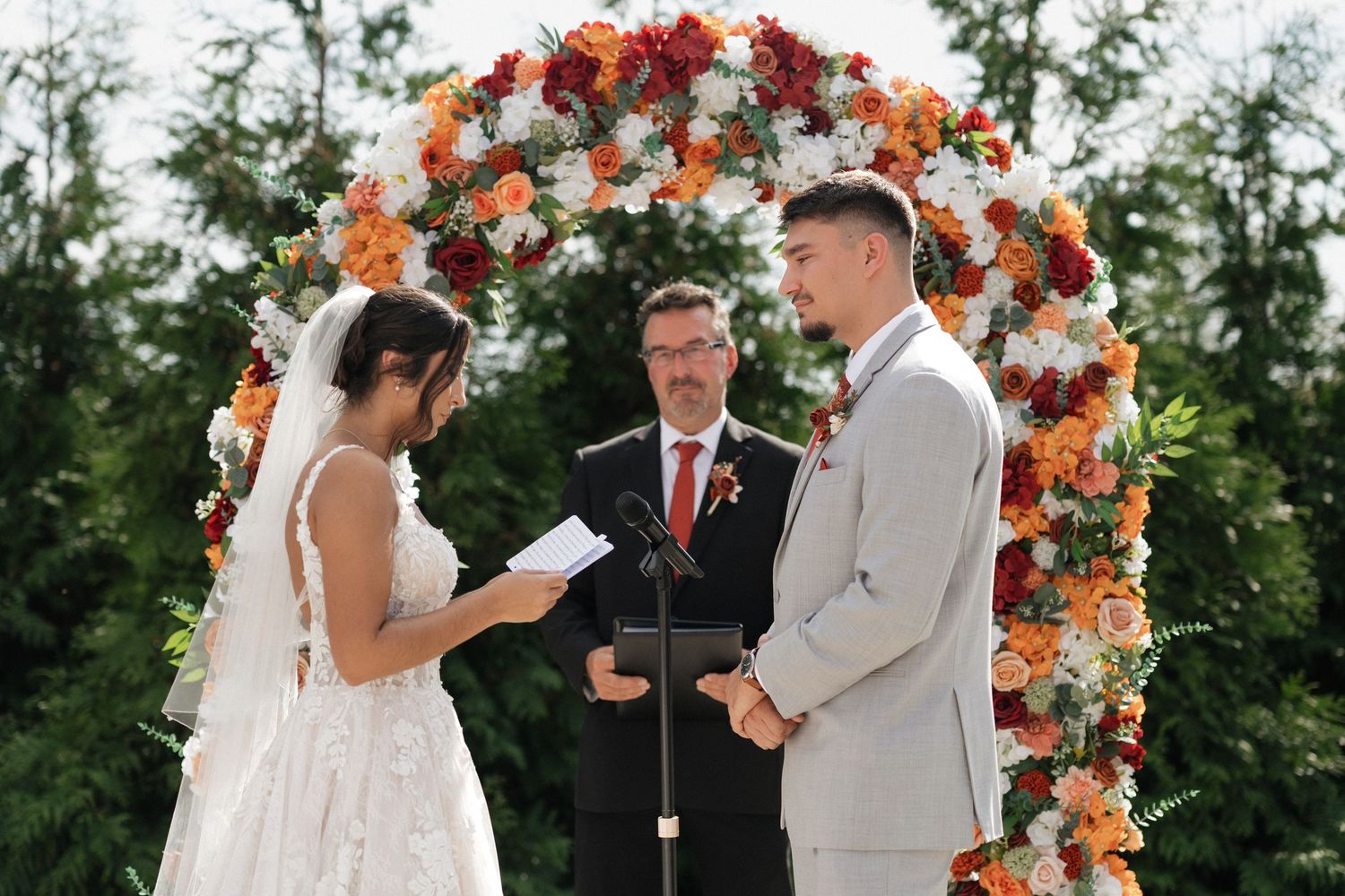 Outdoor wedding ceremony setup with floral arch in orange and peach tones.