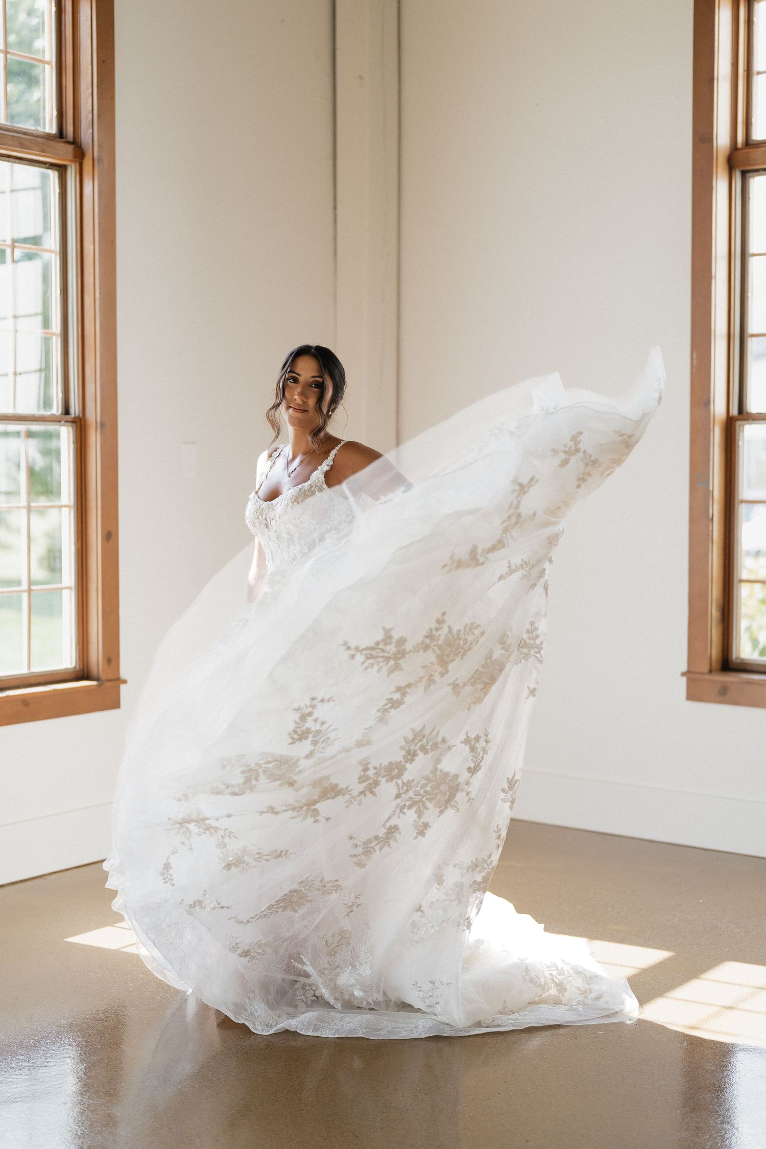 A flowing white lace wedding gown twirls gracefully in natural window light.