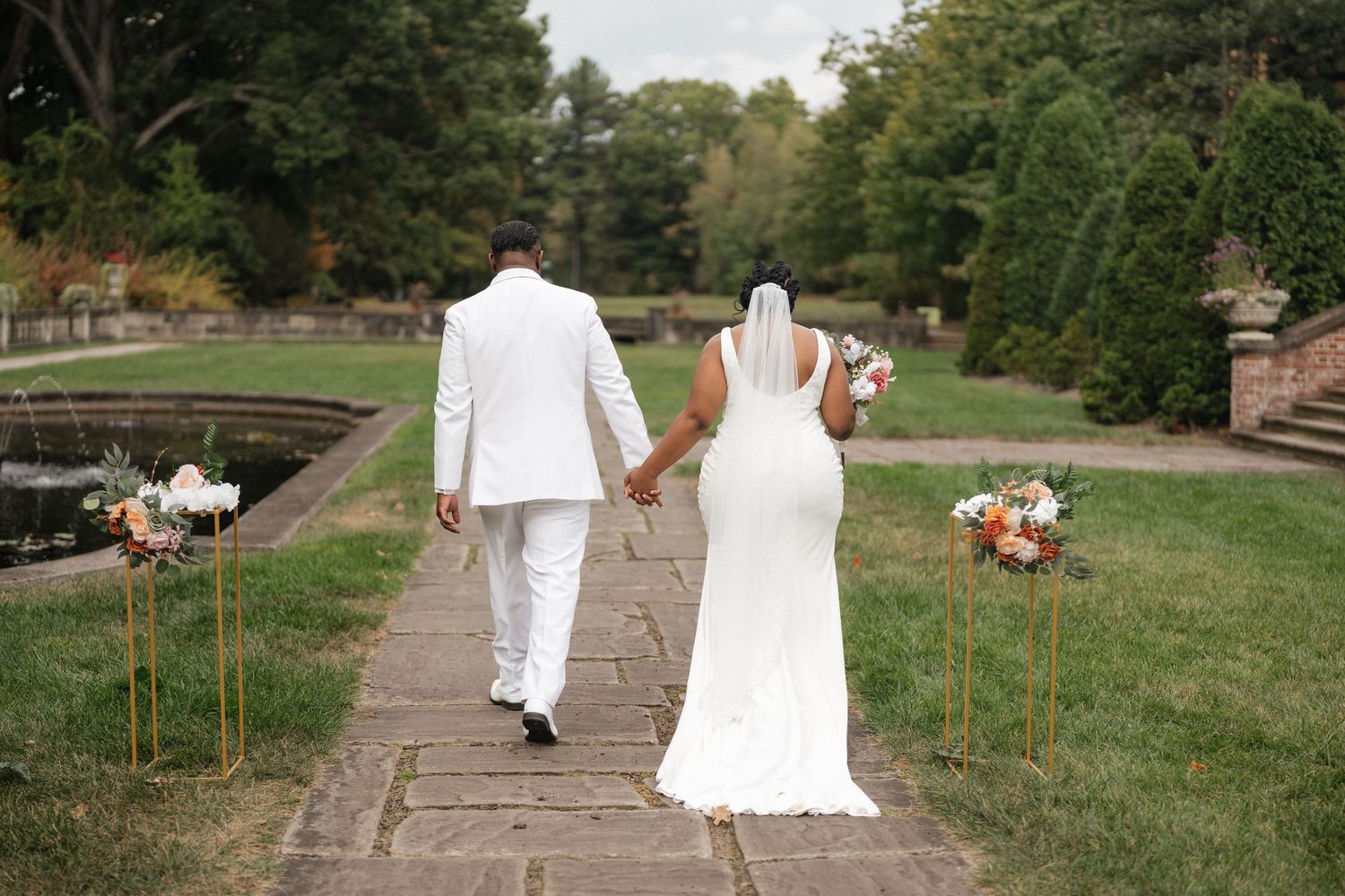 Wedding couple walks along stone steps surrounded by green landscaping.