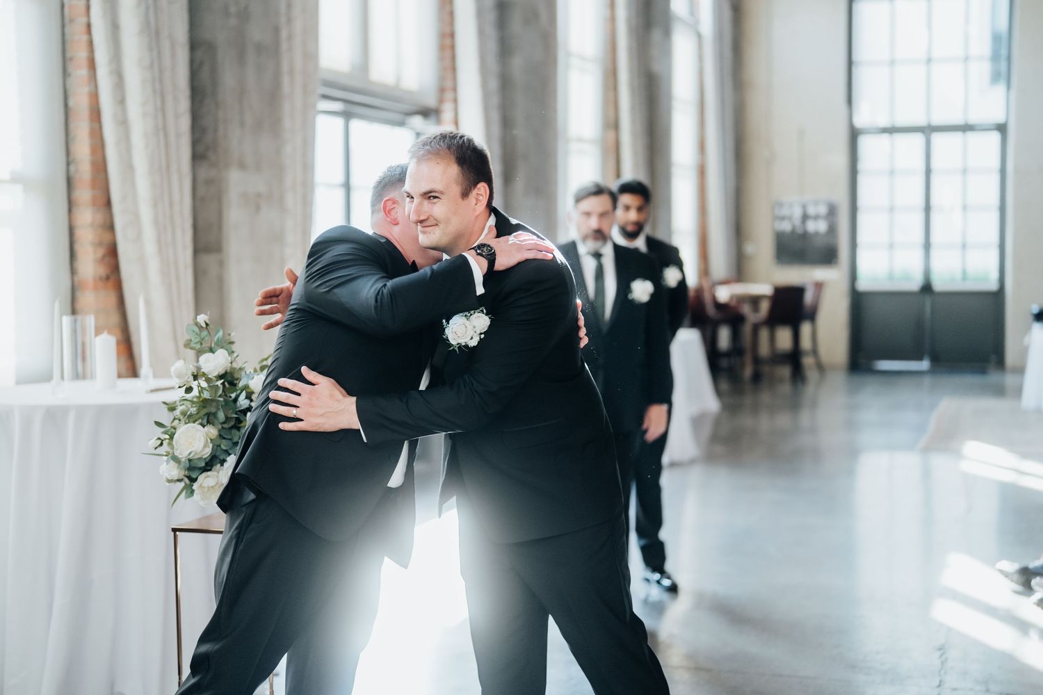 Wedding couple shares their first look moment in a bright industrial venue with large windows.