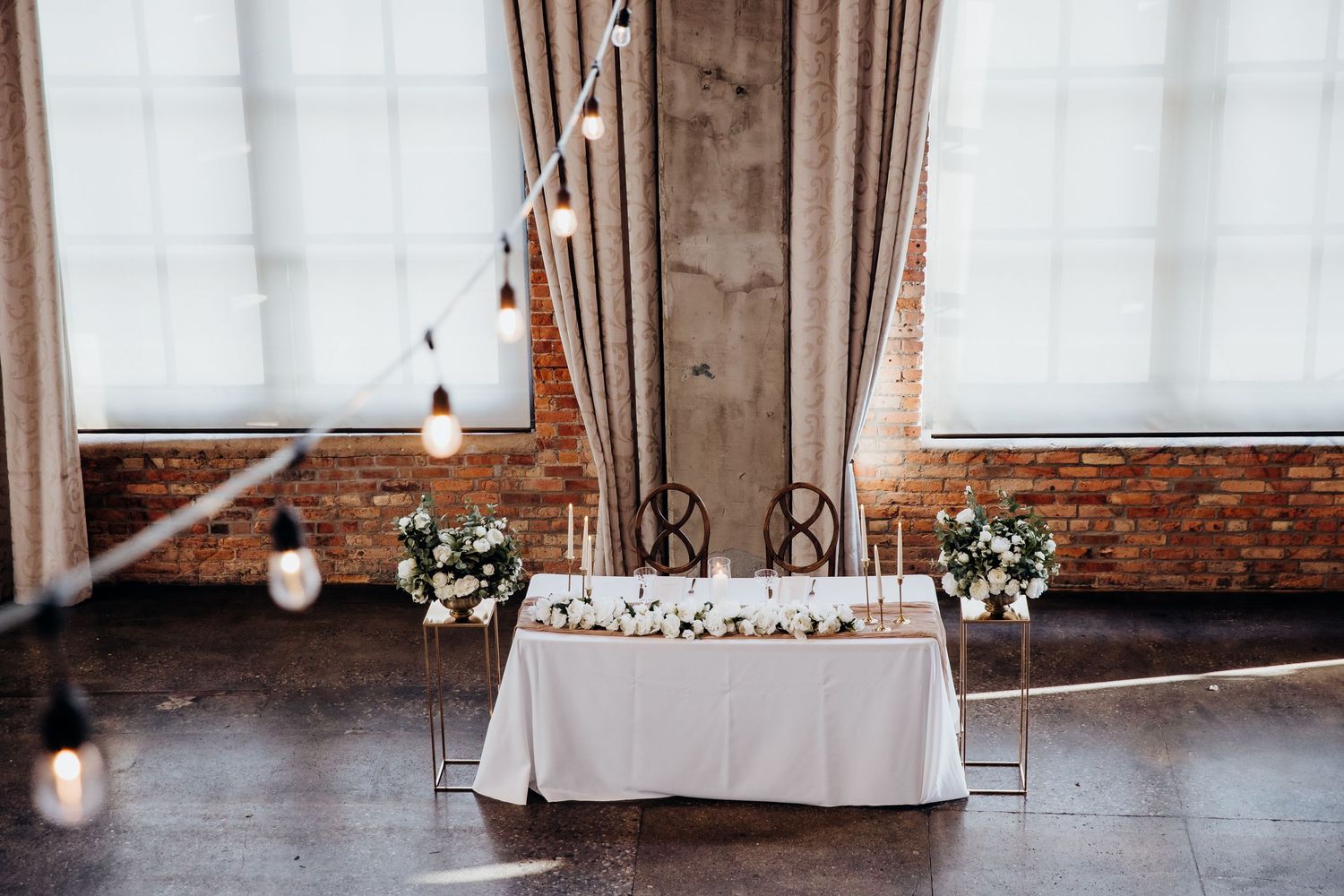 Modern wedding ceremony space with white drapes, exposed brick, and hanging lights.