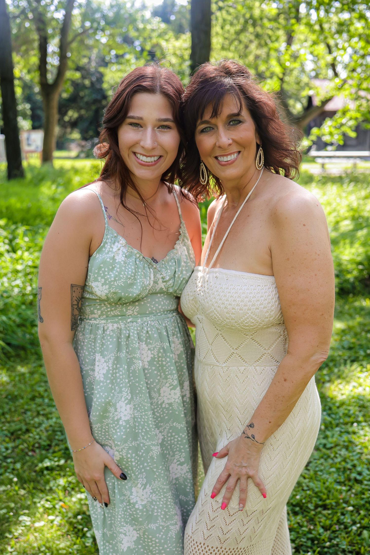 Two people in summer dresses embrace and smile in sunny garden setting.